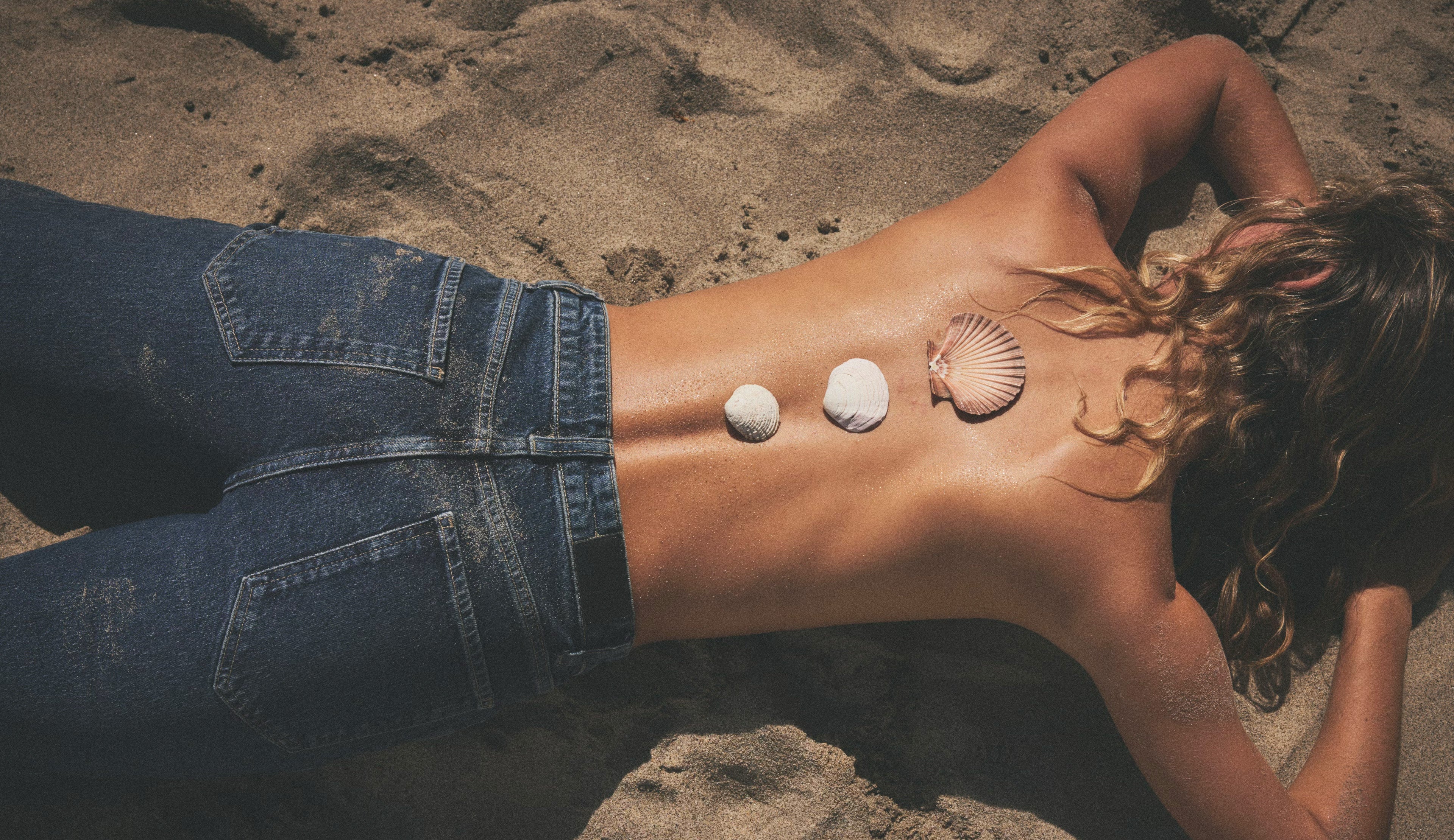 Person lying on sand with three seashells on their back
