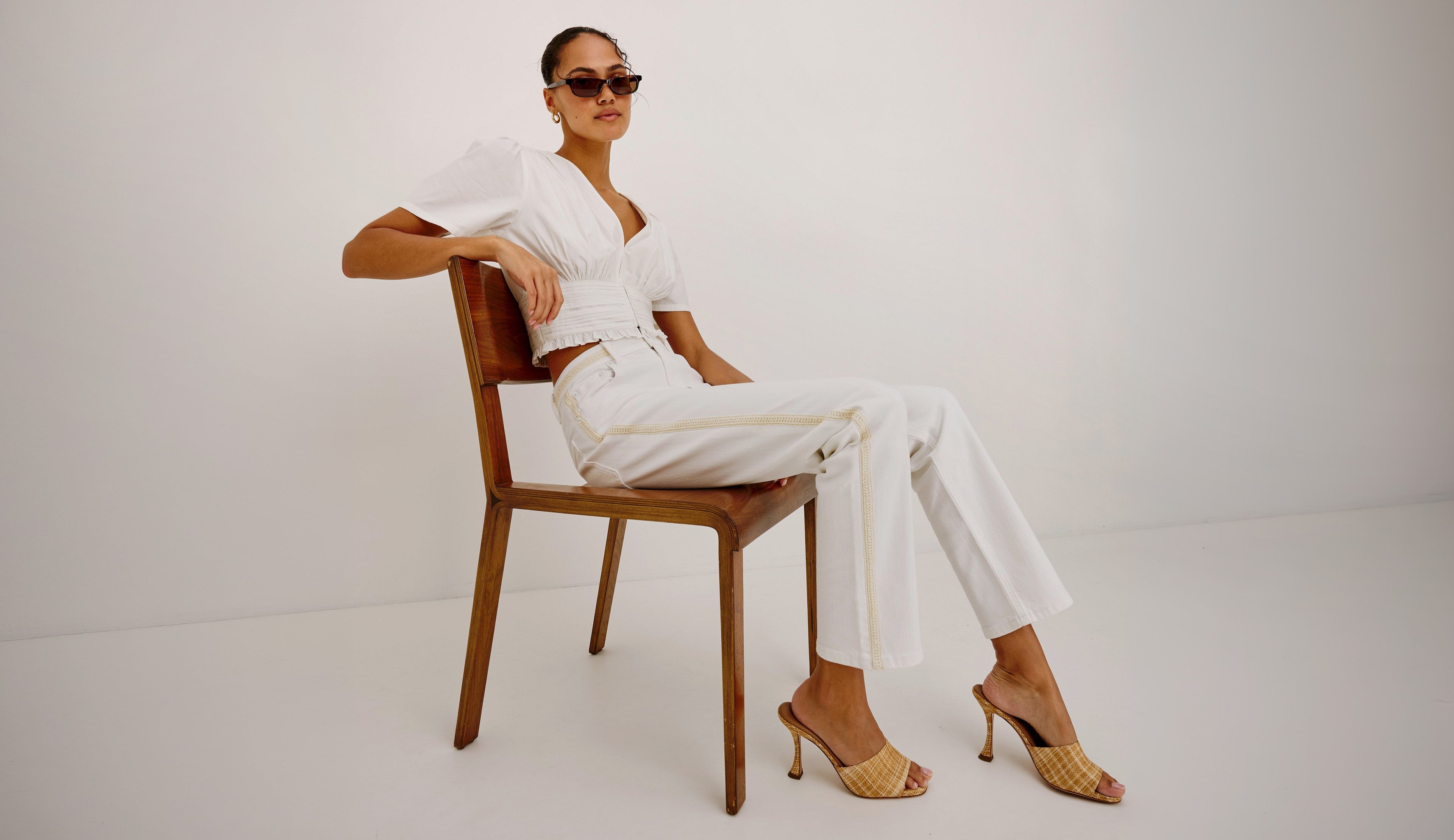 Woman in a white outfit sitting on a wooden chair against a white background