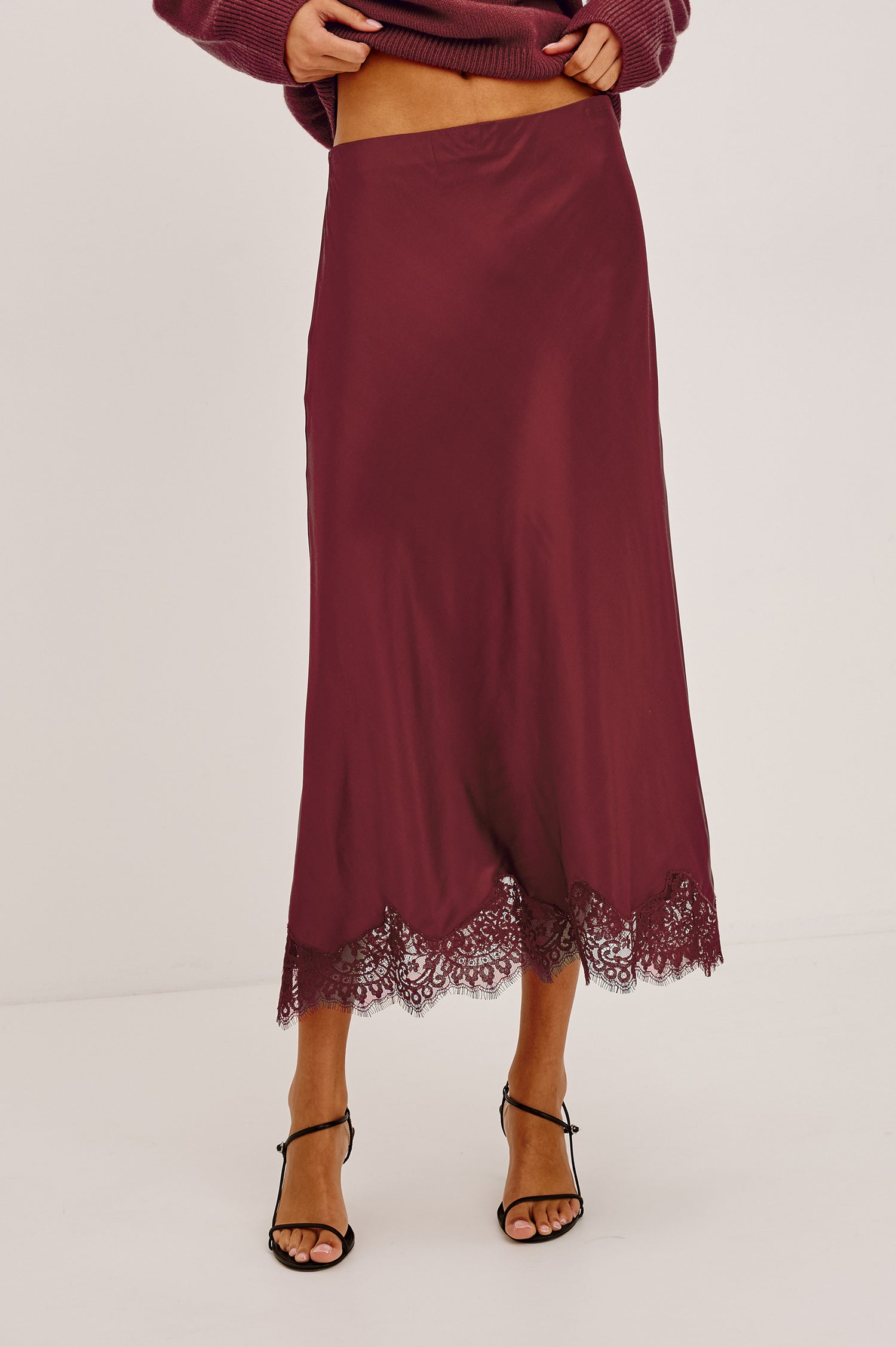 Ebony Midi Skirt Bias Cut in Satin With Clean Elastic Waistband, Pull-On Fit, and Tonal Lace Trim at Hem in Crimson Colorway - Lower Body Front View Featured on Model