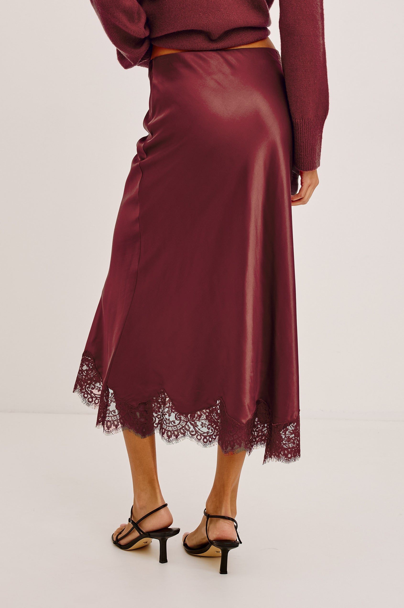 Ebony Midi Skirt Bias Cut in Satin With Clean Elastic Waistband, Pull-On Fit, and Tonal Lace Trim at Hem in Crimson Colorway - Lower Body Back View Featured on Model