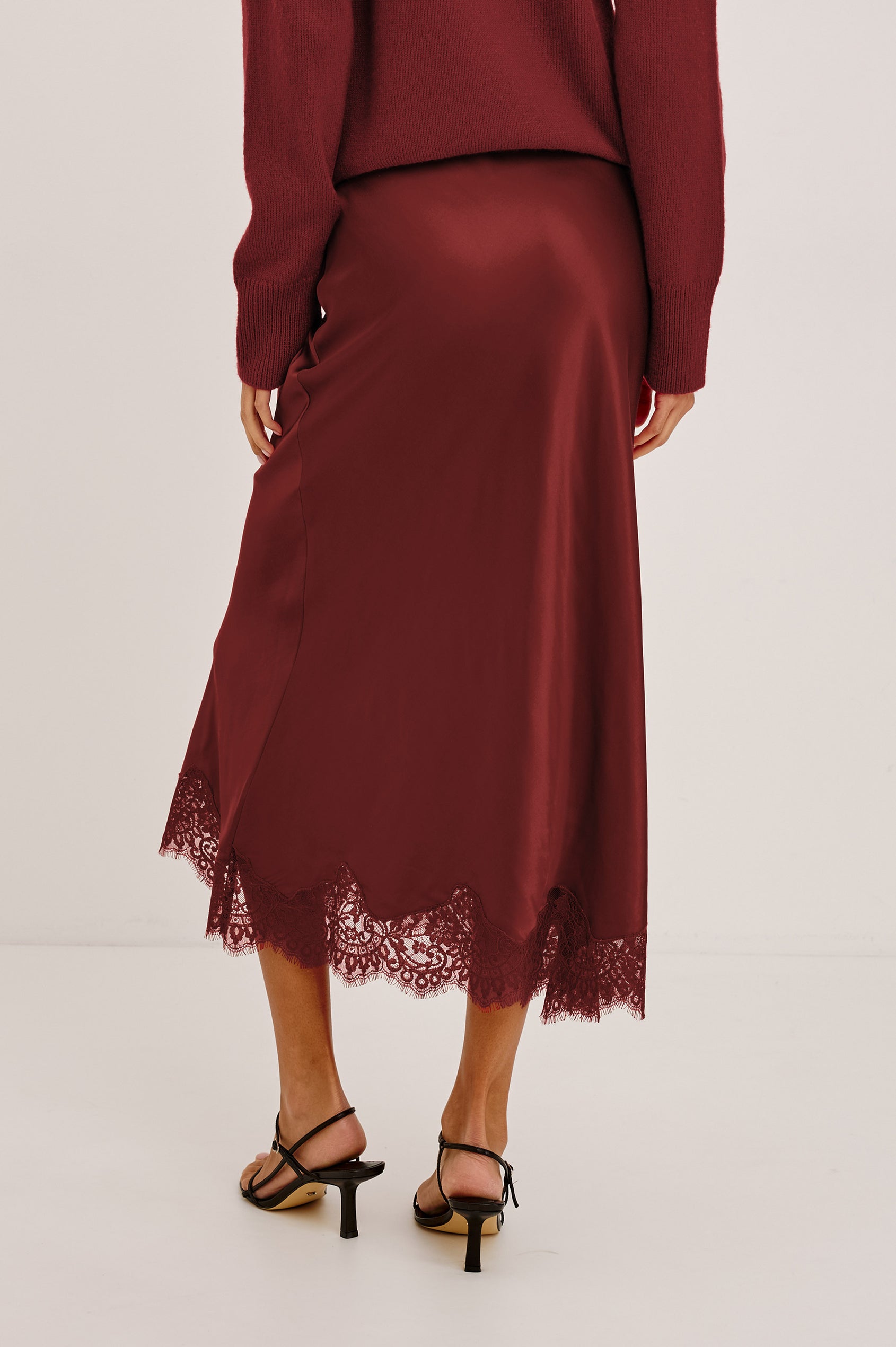 Ebony Midi Skirt Bias Cut in Satin With Clean Elastic Waistband, Pull-On Fit, and Tonal Lace Trim at Hem in Crimson Colorway - Lower Body Back View Featured on Model