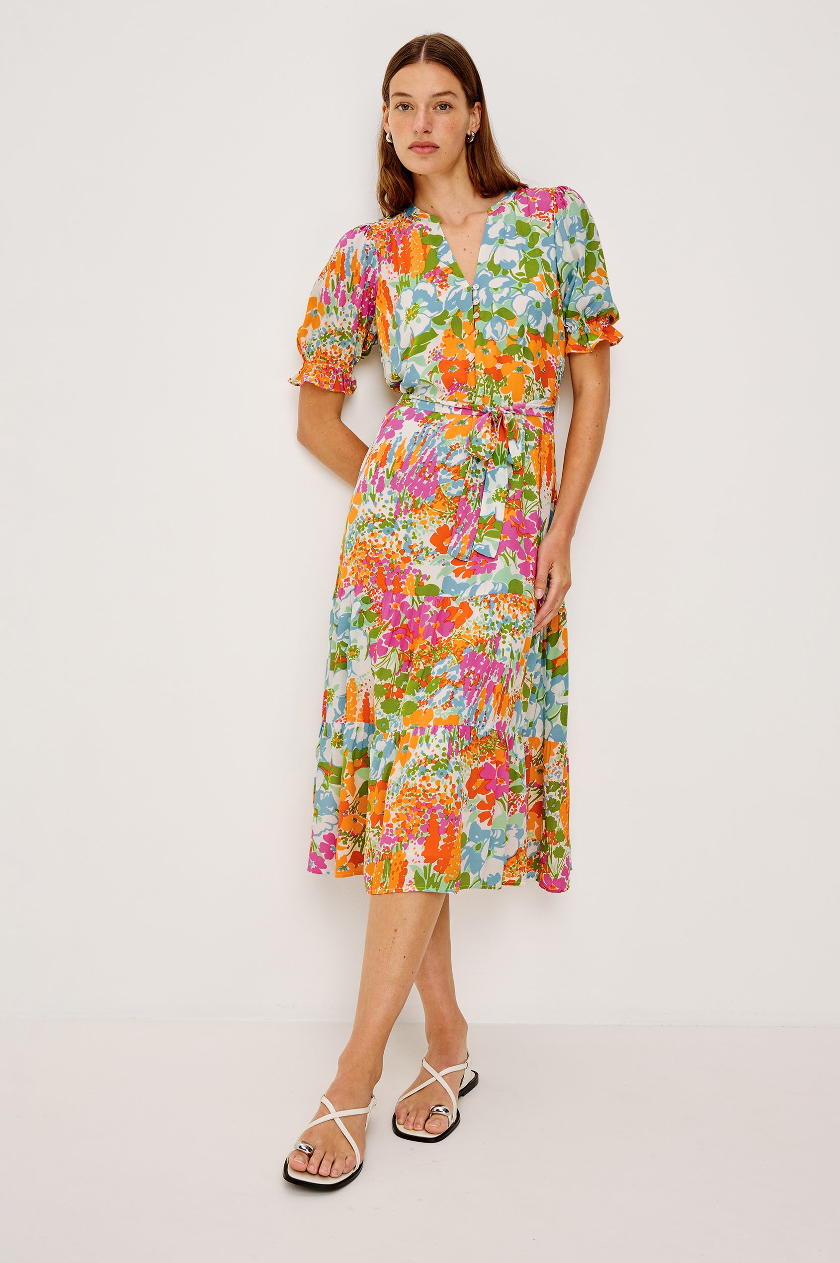 Eliana Midi Dress with Elbow-Length Sleeves with Shirred Cuffs, a V Neck, Buttons Down the Bodice, a Fabric Tie at the Waist  and a Tiered Skirt in Day Garden Colorway, a Floral Pattern in Blue, Pink and Oranges on White - Front Full Body View Featured on Model