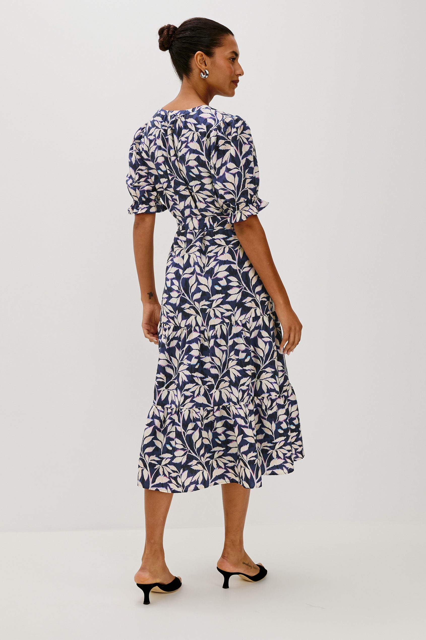 Eliana Midi Dress with Elbow Length Sleeves with Elasticated Ruffle Hem, V-Neck, 3-Button Front, Self Waist Tie and Tiered Skirt in Navy Vines Colorway. Back Full Body View Featured on Model.