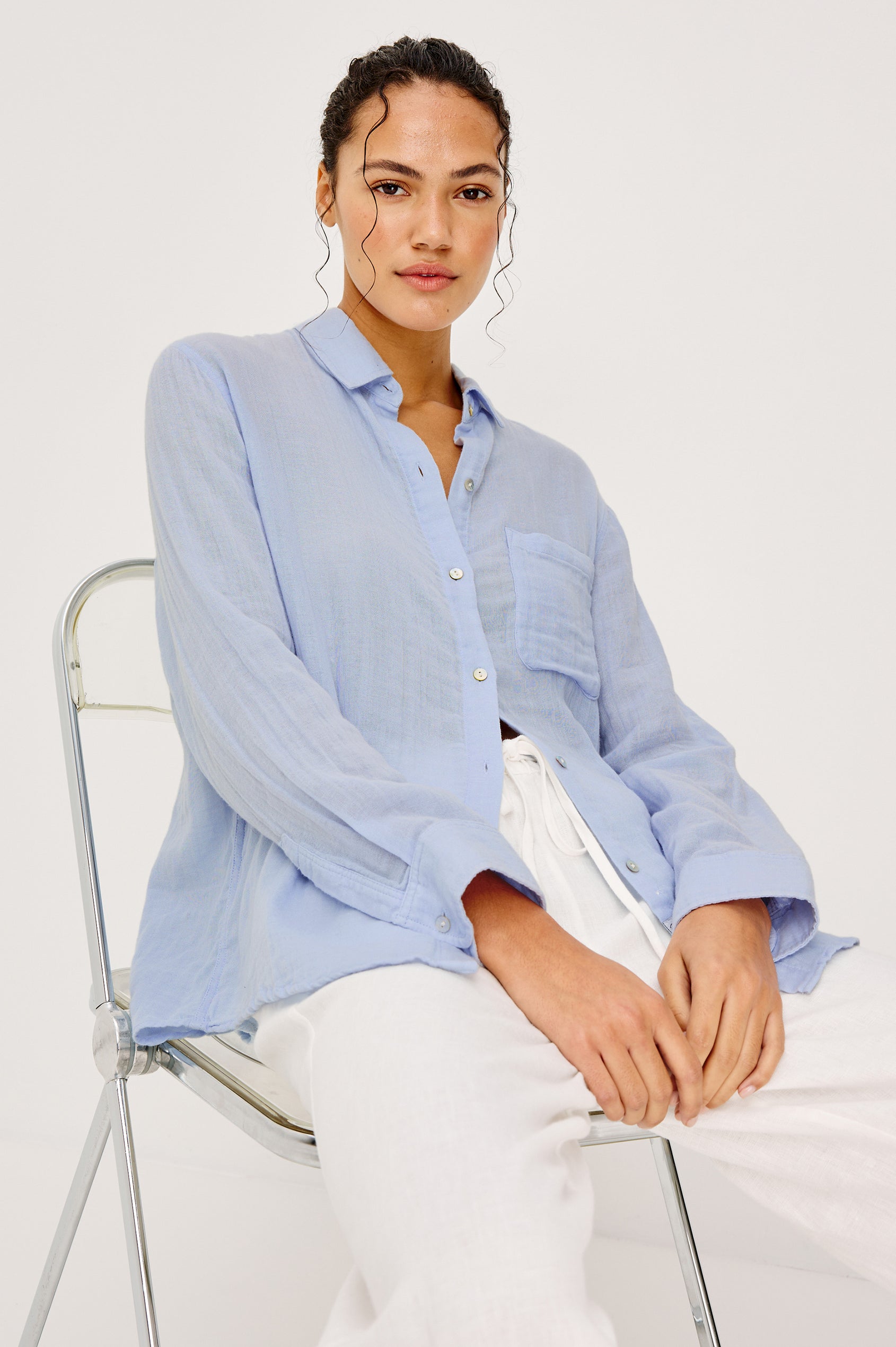 Ellis Relaxed Collared Button Front Shirt with Long Sleeves and a Chest Pocket in Baby Blue Colorway. Upper Body Front View Shown on Model Sitting In A Chair.