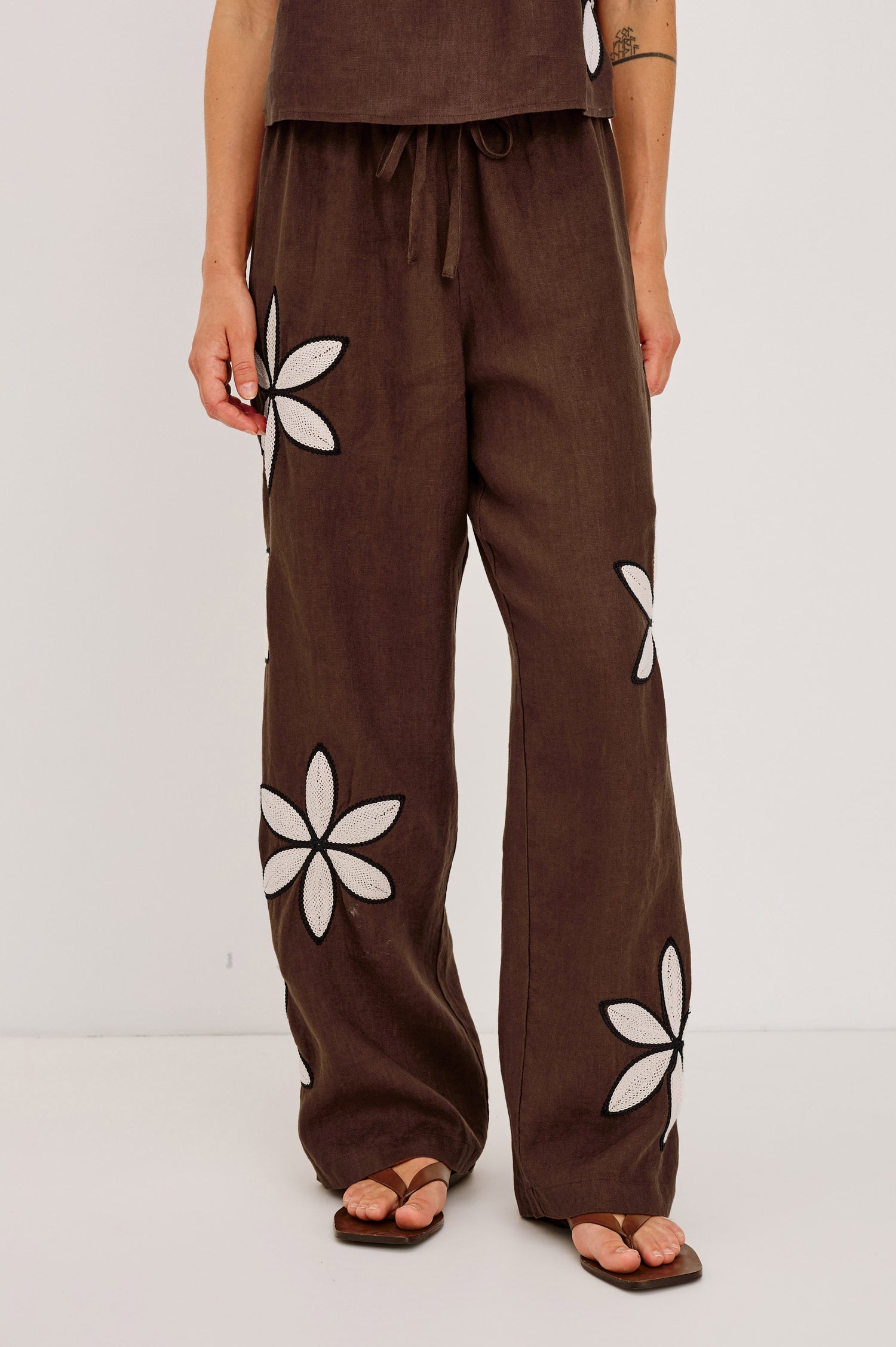 Emmie Straight Leg Pant in Unlined Linen With Adjustable Drawstring Waist Ties and Side Pockets in Cocoa Floral Embroidery Colorway — Lower Body Front View Featured on Model