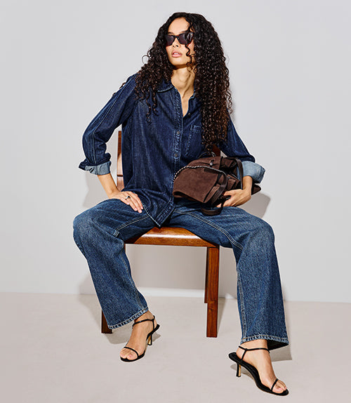 Woman posed on a chair wearing an all denim outfit against a white background.