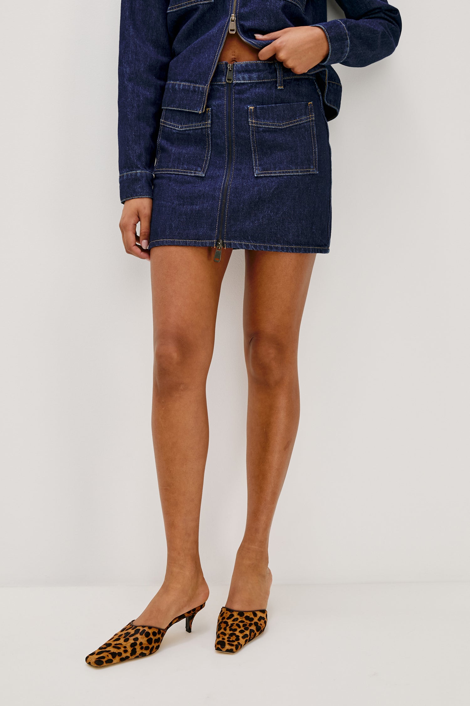 The Fallbrook is a mini zip front denim skirt with beltloops, front patch pockets and back pockets in Deep Indigo colorway. Front view featured on model.