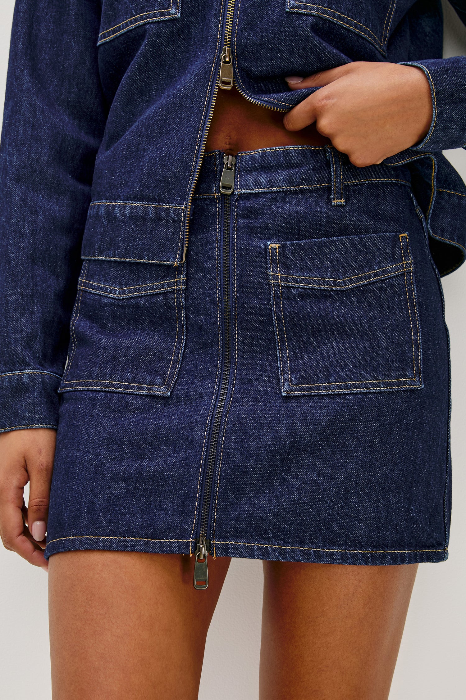 The Fallbrook is a mini zip front denim skirt with beltloops, front patch pockets and back pockets in Deep Indigo colorway. Front detail view featured on model.