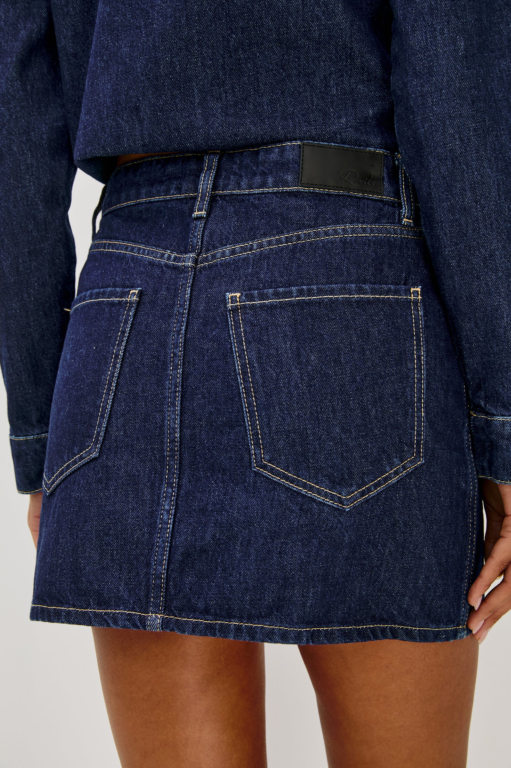 The Fallbrook is a mini zip front denim skirt with beltloops, front patch pockets and back pockets in Deep Indigo colorway. Back view featured on model.
