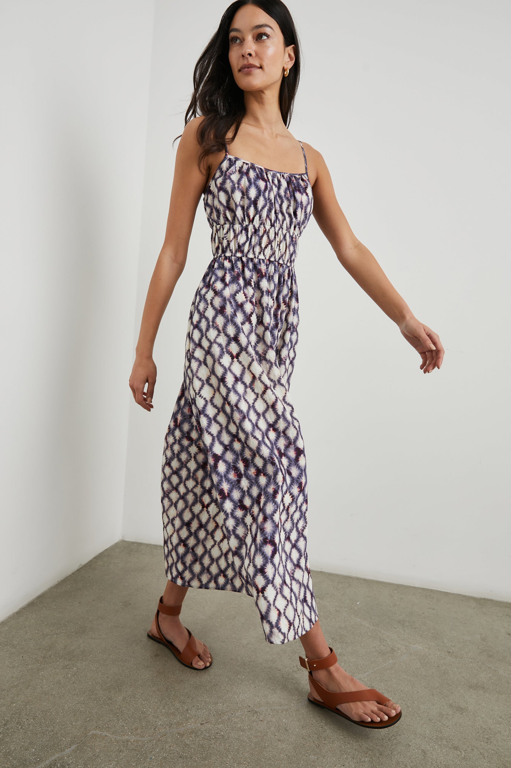 Fatima Sleeveless Mide Dress with a Scoop Neck, Adjustable Spaghetti Straps and a Smocked Waist in Iris Shibori Colorway, a Print in White, Purple and Pinks - Front Full Body View Featured on Model