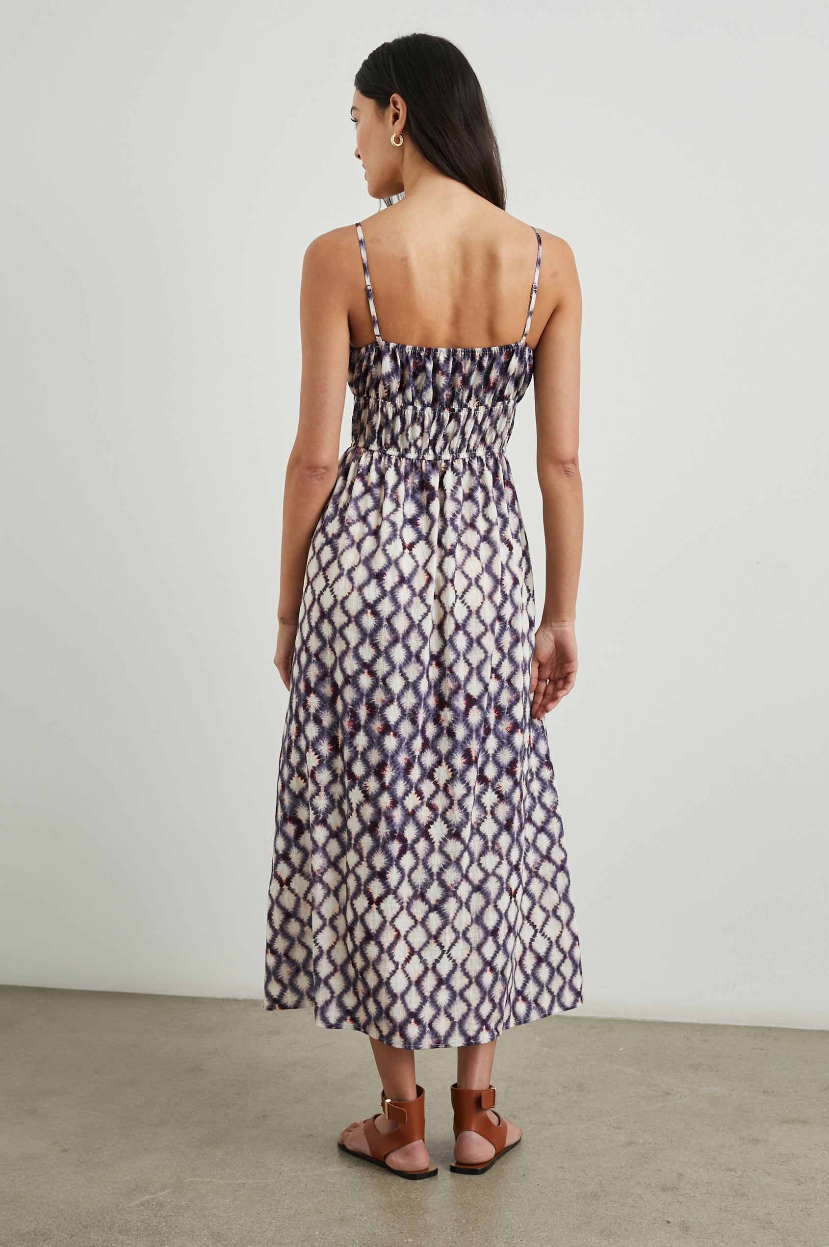 Fatima Sleeveless Mide Dress with a Scoop Neck, Adjustable Spaghetti Straps and a Smocked Waist in Iris Shibori Colorway, a Print in White, Purple and Pinks - Back Full Body View Featured on Model