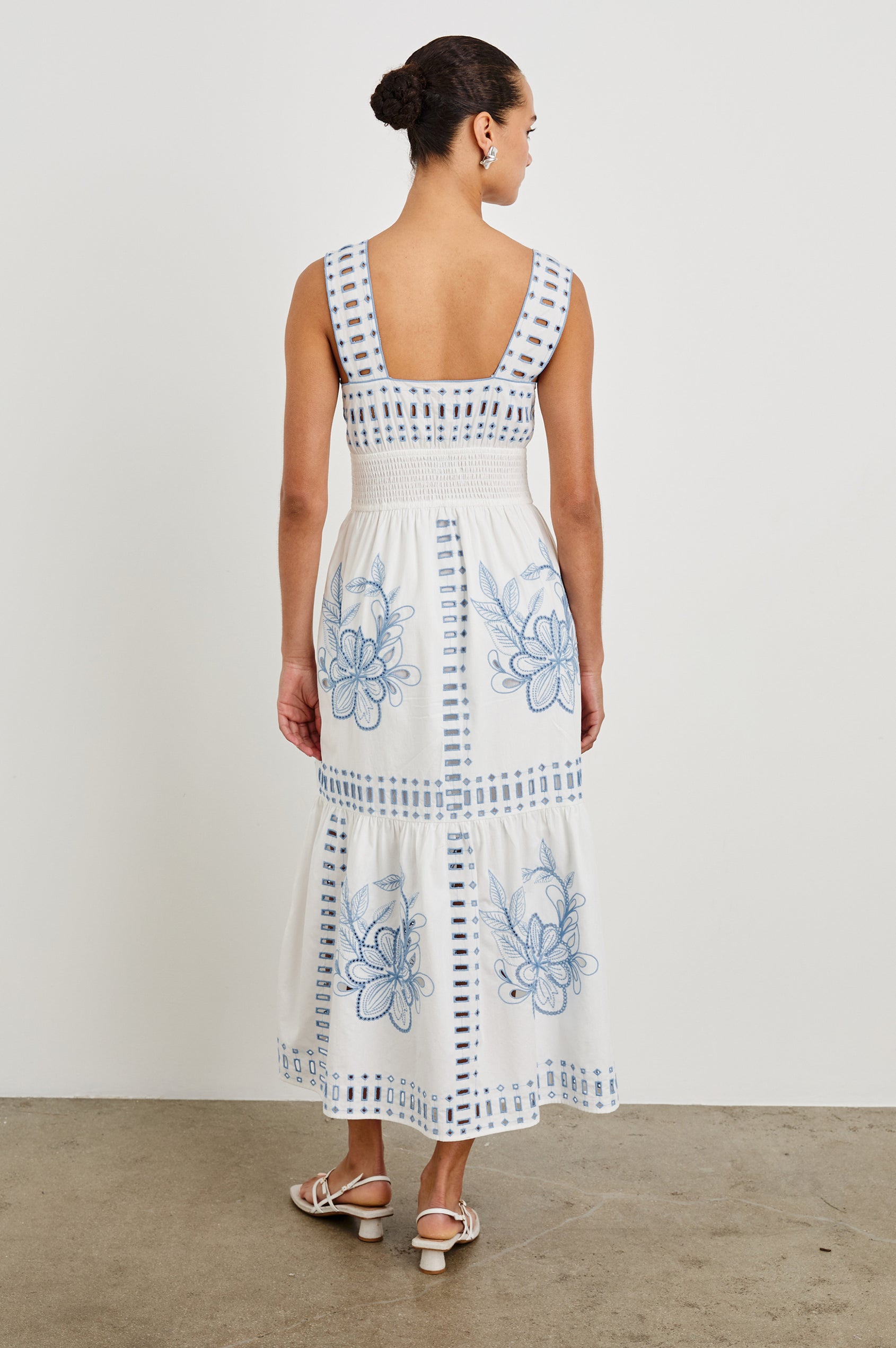 Back view of model wearing our sleeveless, Fawn Midi Dress in White with Blue Embroidery contrast and eyelet details. 