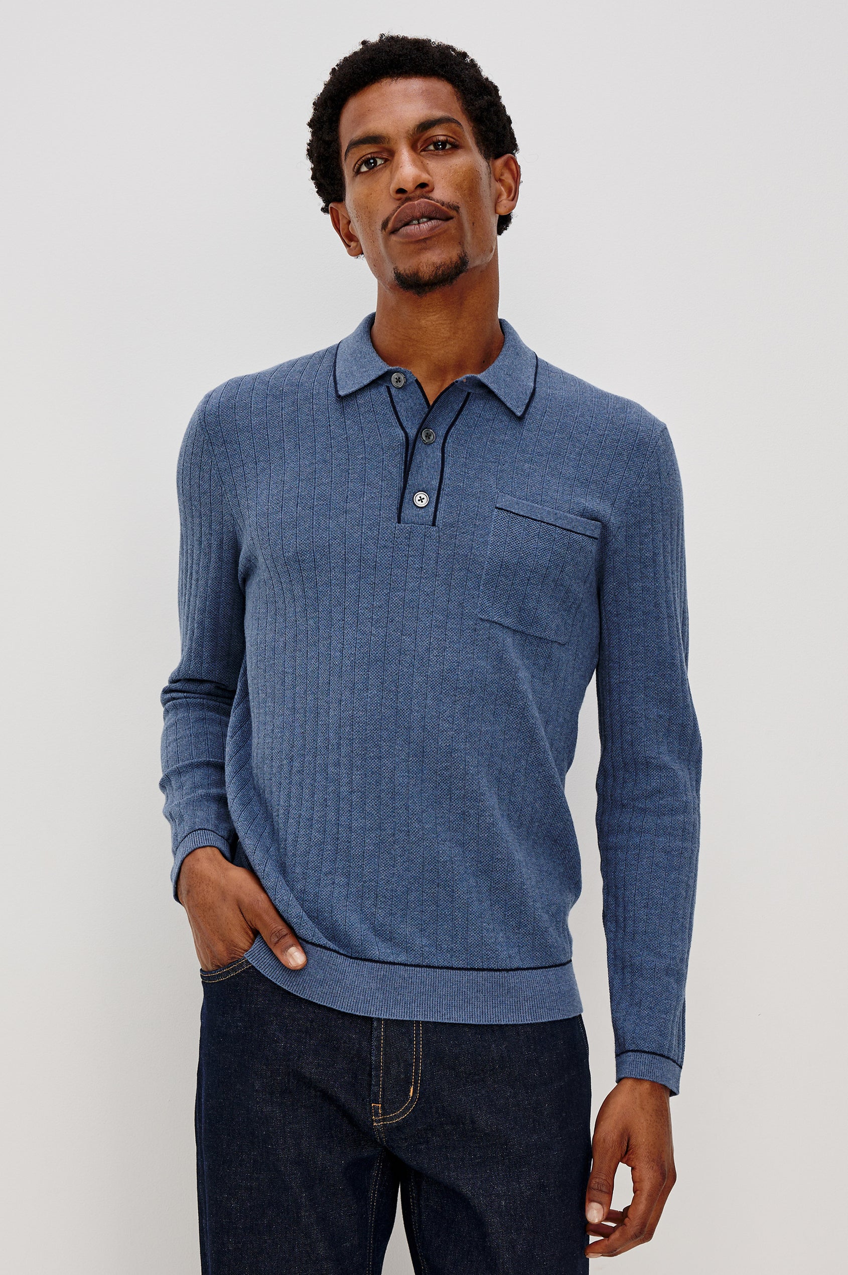 Fenton long sleeve polo sweater with a chest pocket, 3-button placket and collar with dark blue tipping along seam edges in Blue Melange Colorway. Front view of model shown.