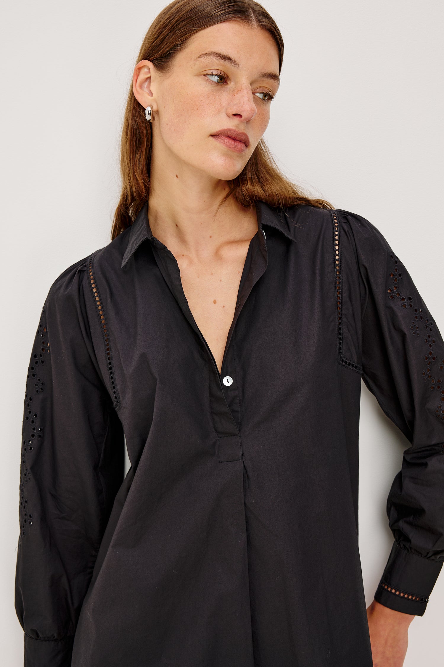 Fernanda Long-Sleeve Mini Dress with Button Cuffs, a Collar, a Placket with Buttons, a Scalloped Hem, a Floral Eyelet Design on the Sleeves and a Floral and Geometric Eyelet Design on the Hem in Black Eyelet Colorway - Close up View Featured on Model