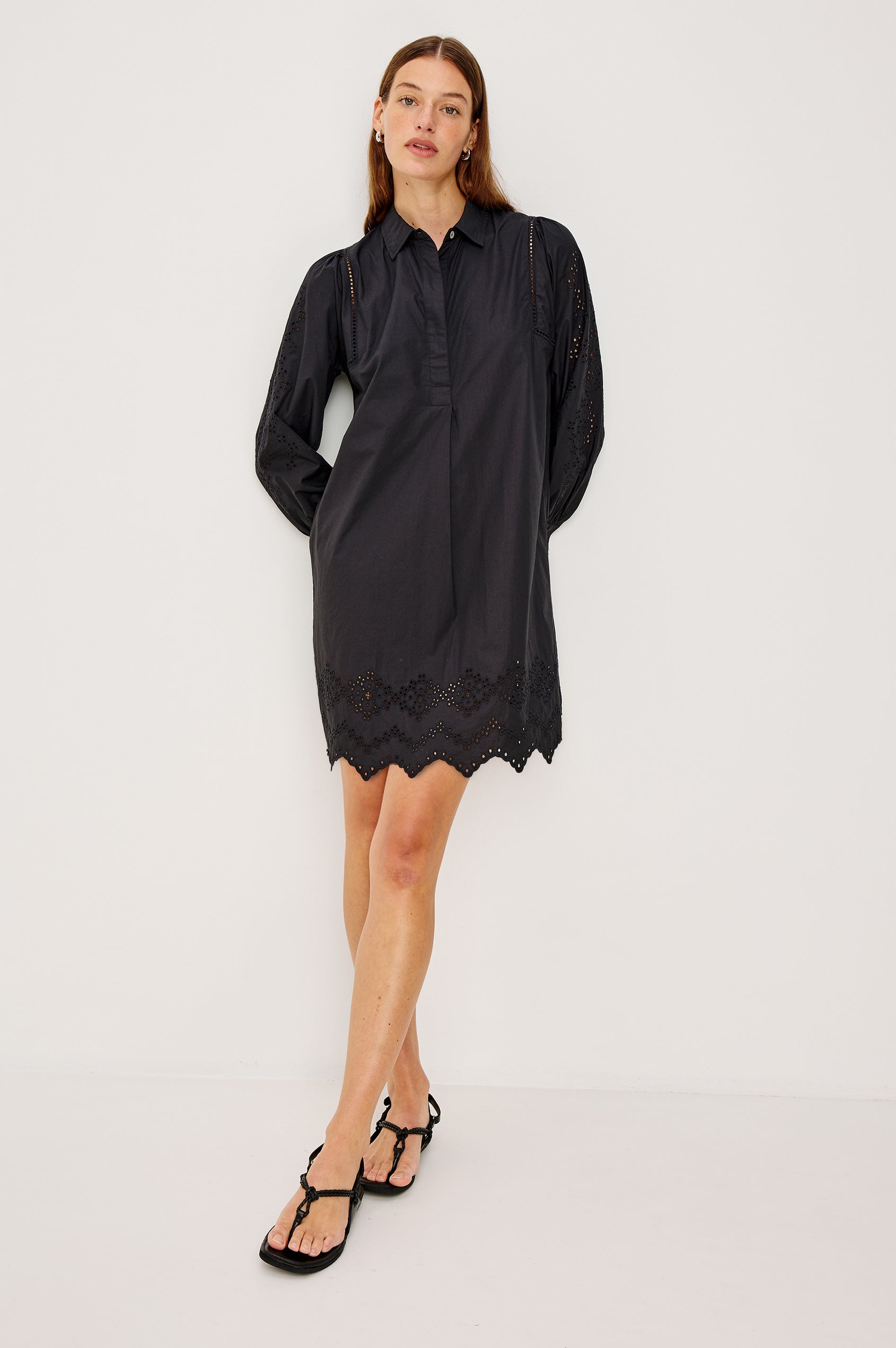 Fernanda Long-Sleeve Mini Dress with Button Cuffs, a Collar, a Placket with Buttons, a Scalloped Hem, a Floral Eyelet Design on the Sleeves and a Floral and Geometric Eyelet Design on the Hem in Black Eyelet Colorway - Full Body Front View Featured on Model