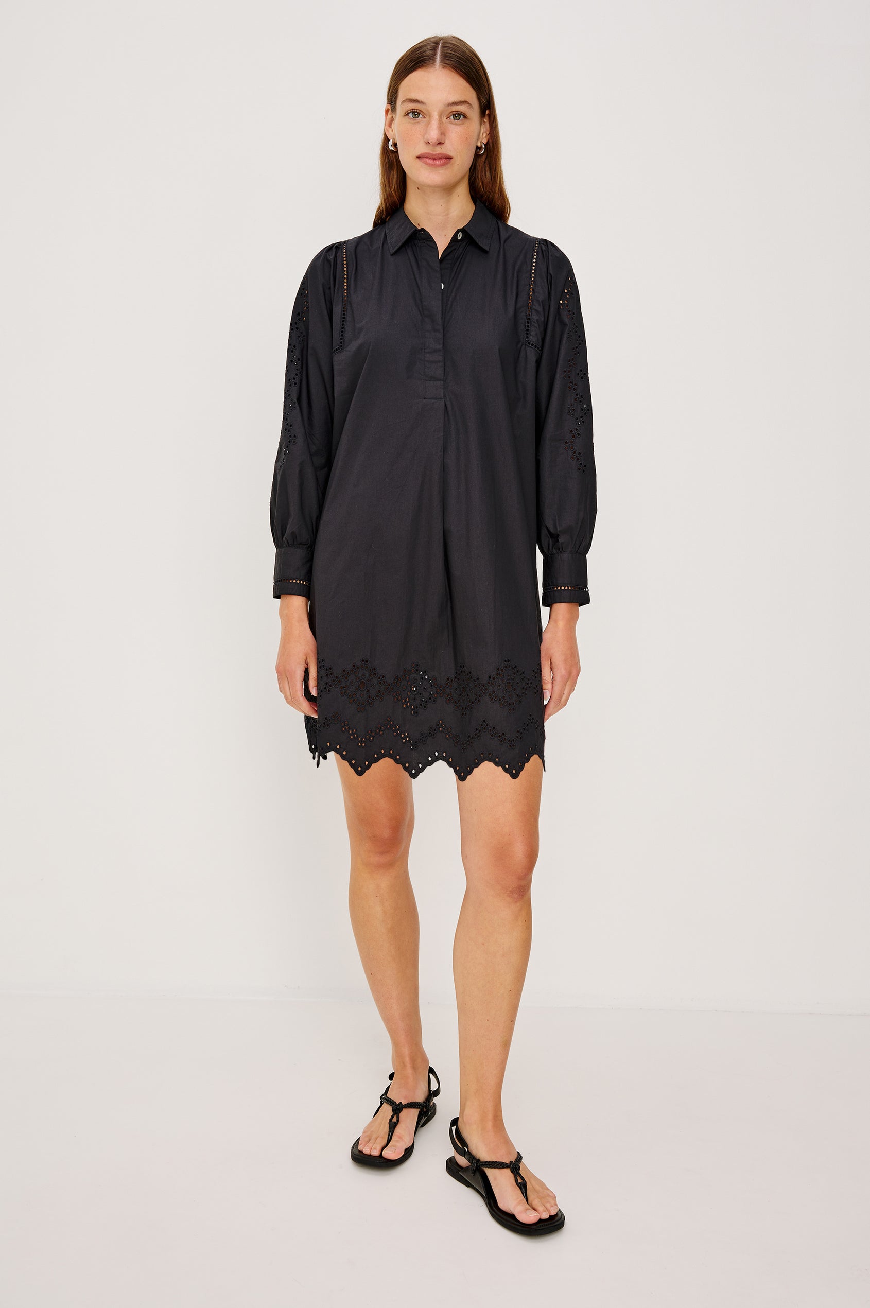 Fernanda Long-Sleeve Mini Dress with Button Cuffs, a Collar, a Placket with Buttons, a Scalloped Hem, a Floral Eyelet Design on the Sleeves and a Floral and Geometric Eyelet Design on the Hem in Black Eyelet Colorway - Full Body Front View Featured on Model