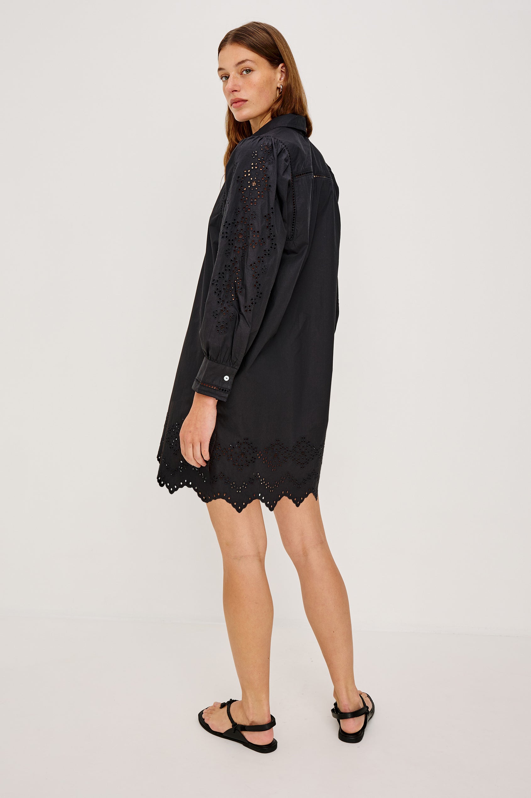Fernanda Long-Sleeve Mini Dress with Button Cuffs, a Collar, a Placket with Buttons, a Scalloped Hem, a Floral Eyelet Design on the Sleeves and a Floral and Geometric Eyelet Design on the Hem in Black Eyelet Colorway - Back View Featured on Model