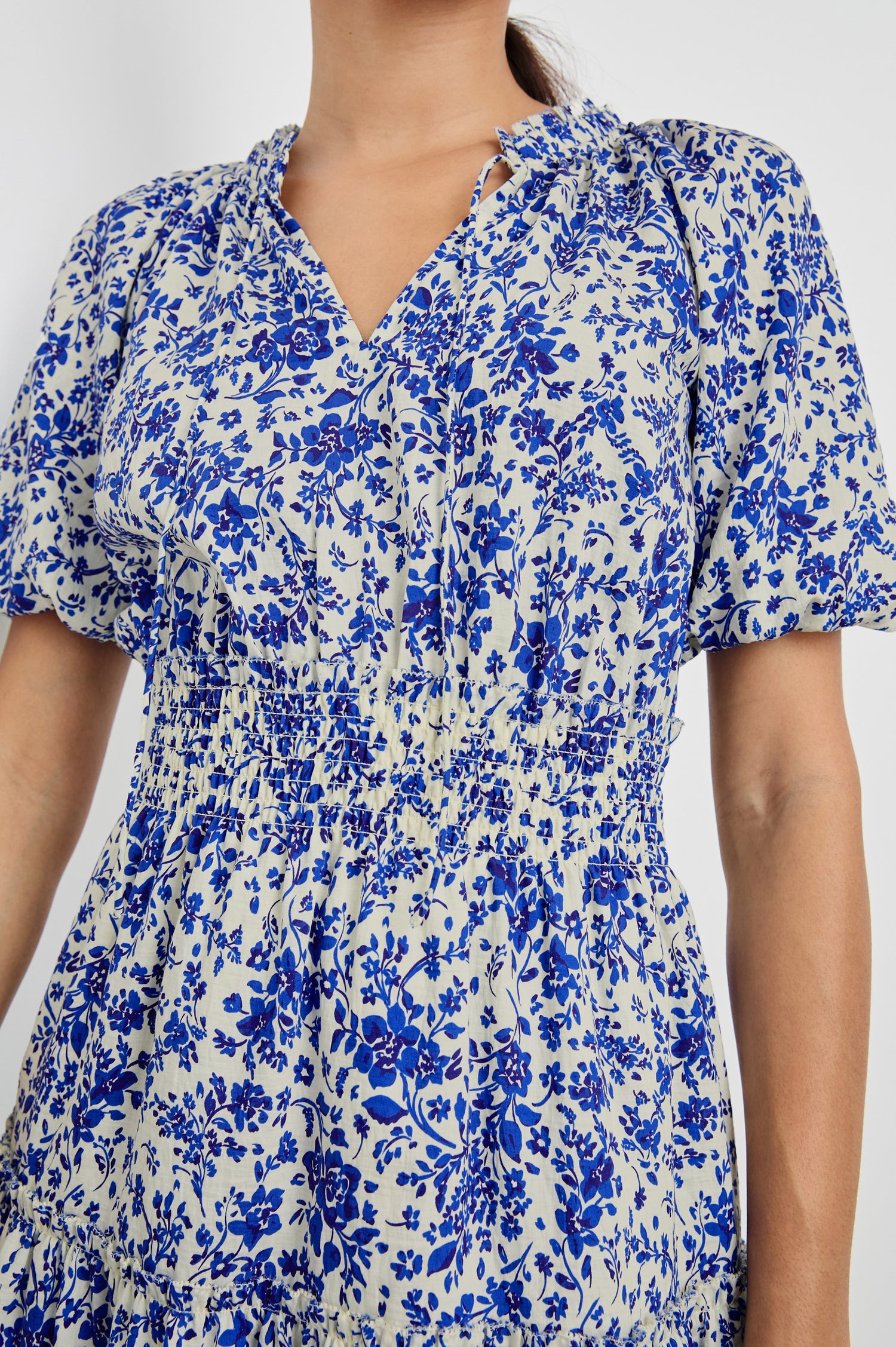 Fiorella Above-Knee Dress with Short Elasticated Puff Sleeves, Split V-Neck with Self Ties, and an Elasticated Ruched Waist Detail in Blue Marguerite Colorway. Front Detailed View Shown on Model.