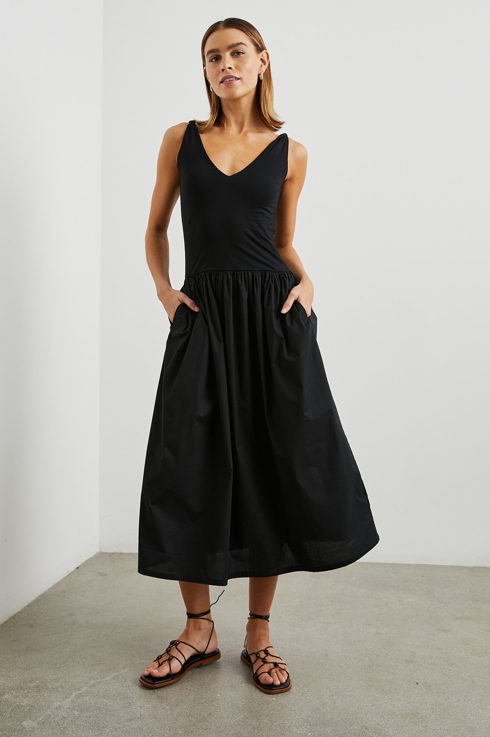 Franca Sleeveless Midi Dress with Twisted Shoulder Straps, a deep V Neck and Pleats at the Waist in Black Colorway - Front Full Body View Featured on Model