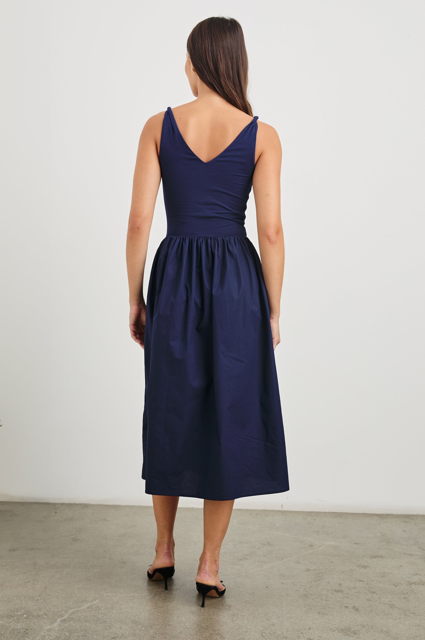 Franca Sleeveless Midi Dress with Twisted Shoulder Straps, a deep V Neck and Pleats at the Waist in Navy Colorway - Back Full Body View Featured on Model