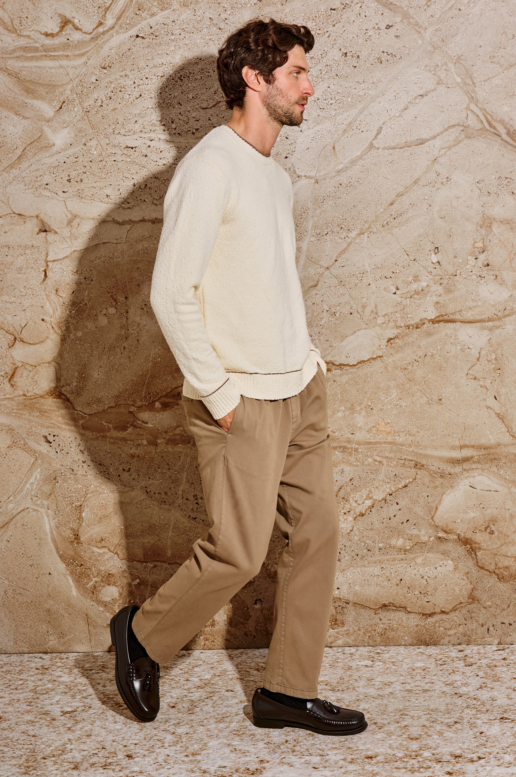The Franco is a long sleeve crew neck sweater with contrast brown on neck, sleeve and hem in Cream colorway. Side full body view featured on model.