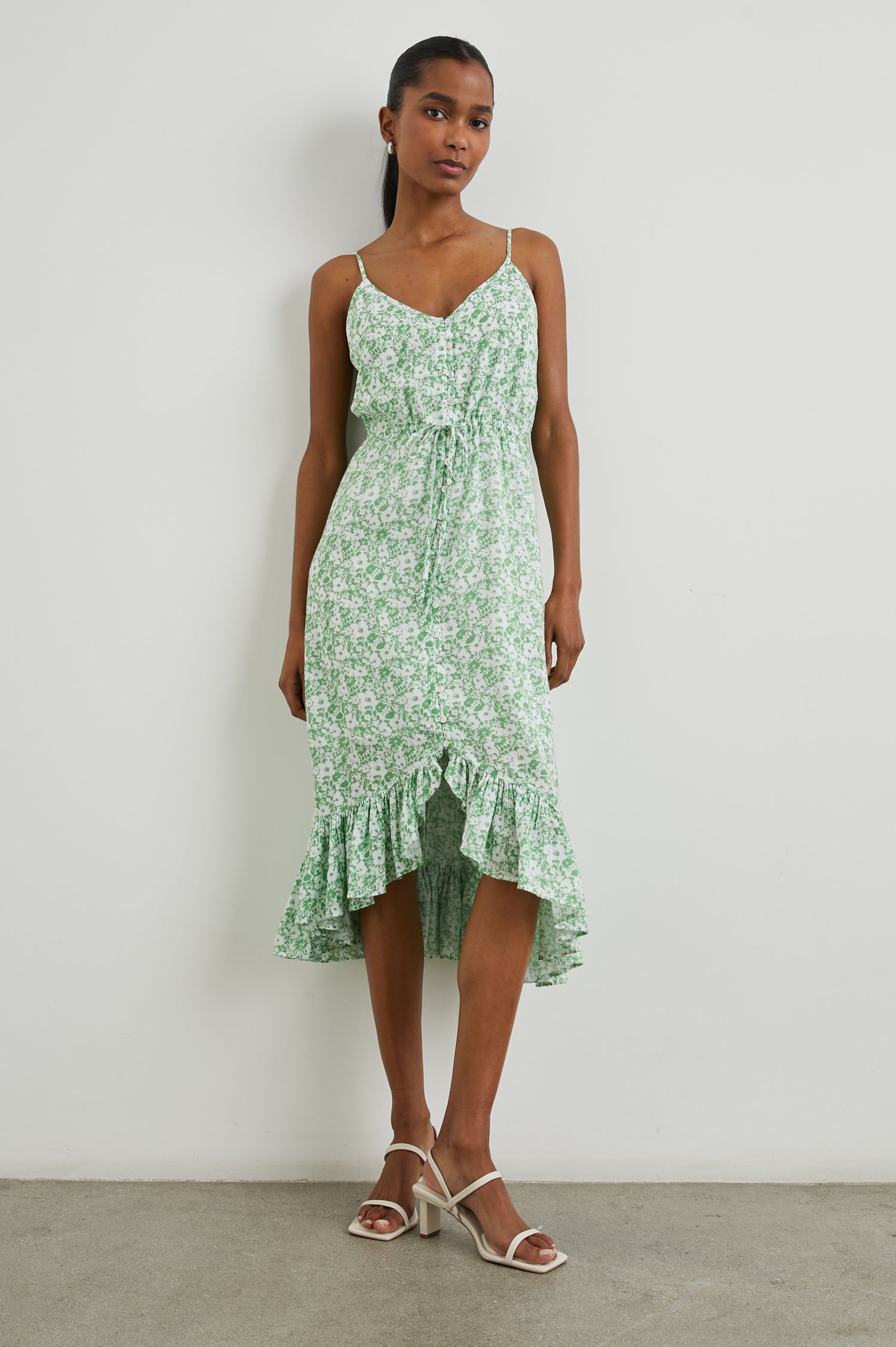 Frida Midi Dress with a Deep V Neck, Adjustable Spaghetti Straps, a Ruffled Hem, Drawstring Waist Ties and Buttons Down the Front in Green Texture Floral Colorway, Green and White Flowers - Front Full Body View Featured on Model