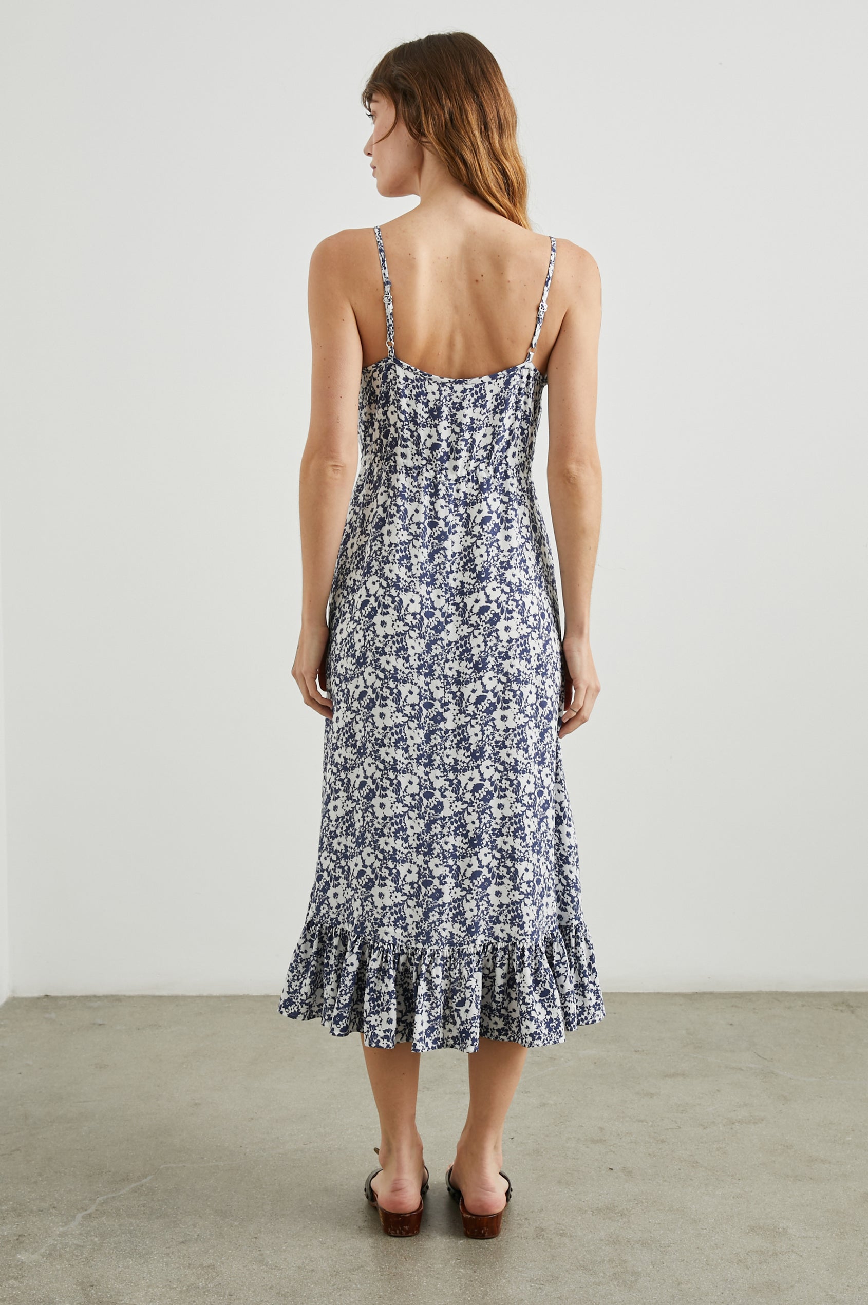 Frida Midi Dress with a Deep V Neck, Adjustable Spaghetti Straps, a Ruffled Hem, Drawstring Waist Ties and Buttons Down the Front in Navy White Texture Floral Colorway - Back Full Body View Featured on Model