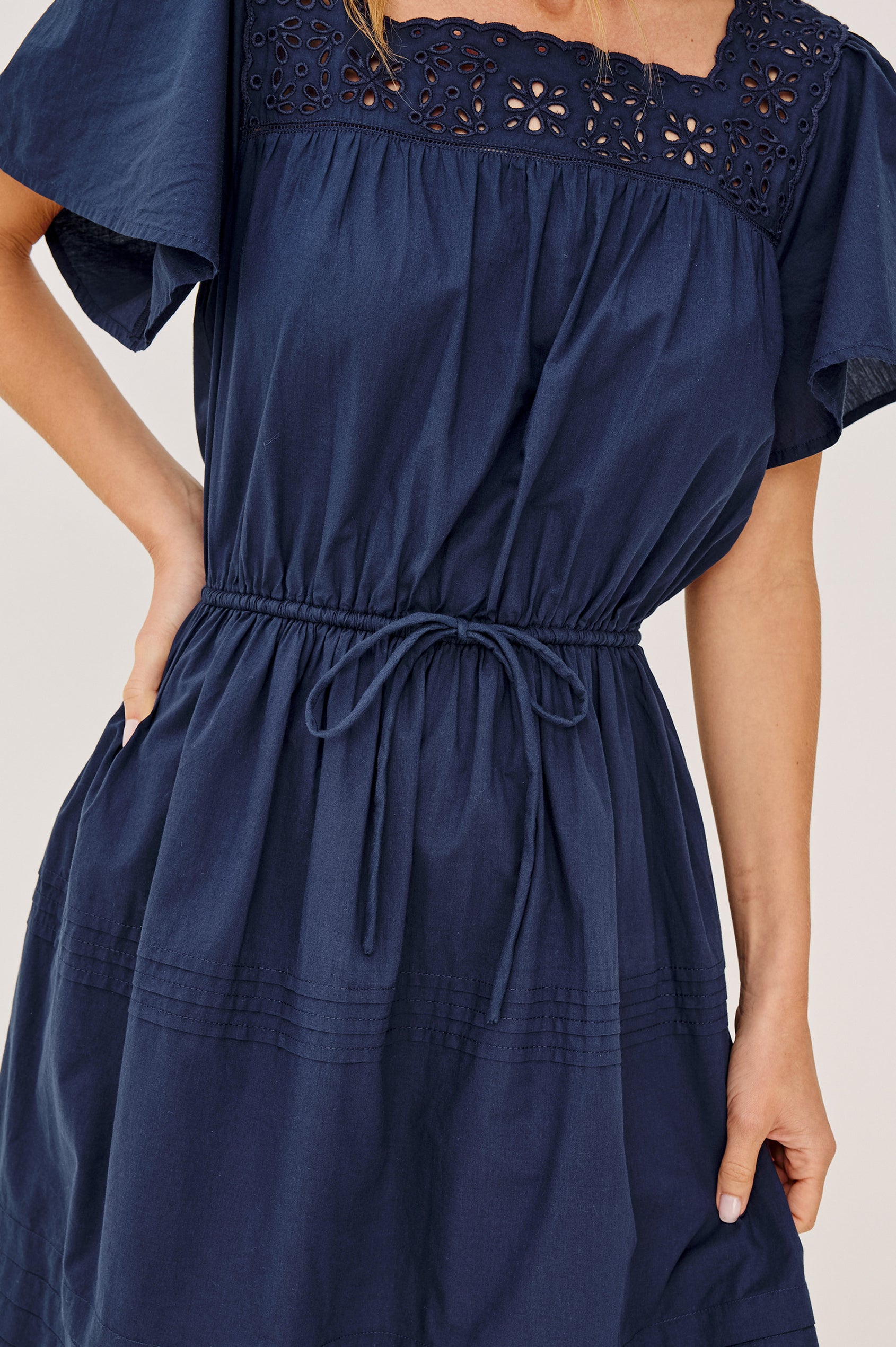 Gale Mini Dress in Cotton Voile With Embroidered Square Neckline, Drawstring Waist Ties, Short Flutter Sleeves, Pintuck Detailing, and Lined Skirt in Navy Colorway - Full Body Back View Featured on Model
