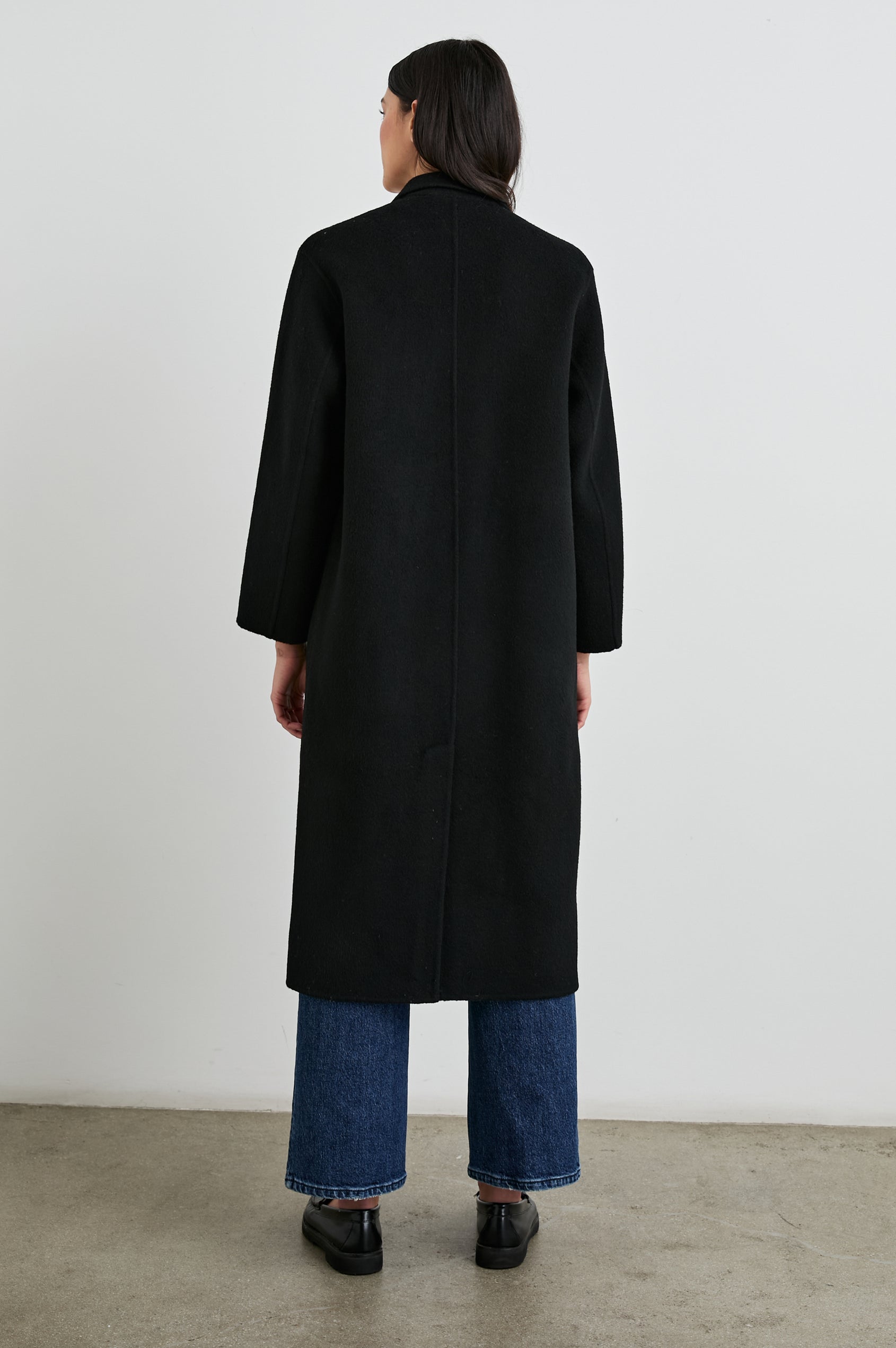 Gallery Below-the-Knee Coat with Three-Button Closure, Notched Lapels, and Two Front Flap Pockets in Black Colorway - Back Full Body View Featured on Model