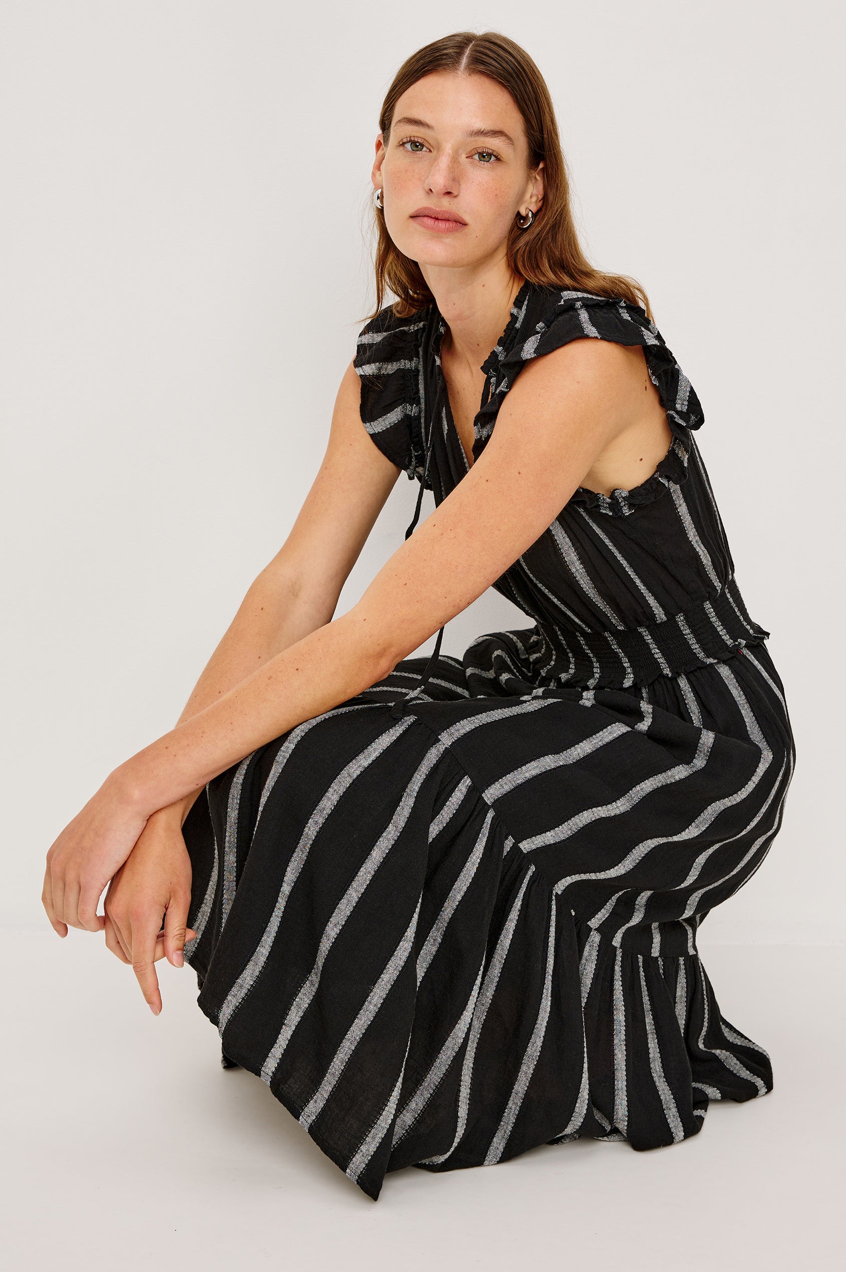 Garden Midi Dress with Flutter Cap Sleeves, Drawstrings at V-Neck and Shirred Waistband in Ash Leno Stripe Colorway, with Grey Vertical Stripes on Black - Front View Featured on Model with Model in Squatting Position