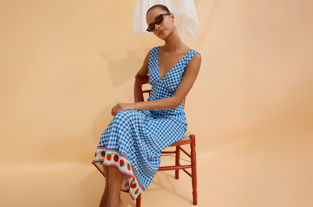Woman in a blue checkered dress sitting on a chair against a beige background