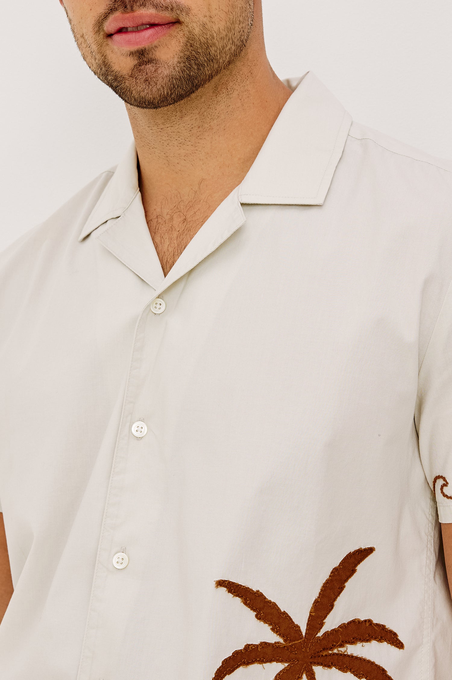 Gibson Button-Up Shirt in Stretch Linen Blend With Short Sleeves, Notched Collar, and Palm Tree Embroidery in Natural Sunset Colorway - Upper Body Front Close Up View Featured on Model