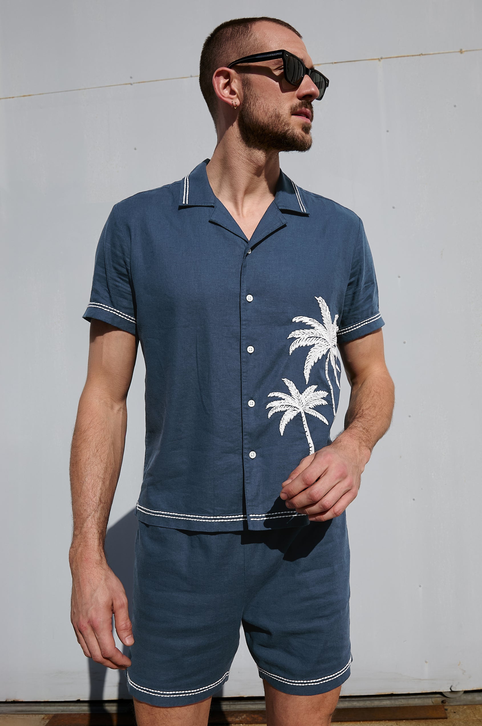 Gibson Button Front Shirt with Open Relaxed Collar, Short Sleeves, White Contrast Buttons, Contrast White Stitching at Collar and Hems and Embroidered White Palm Trees on Left Side in Navy White Palm Colorway. Front View Shown on Model.