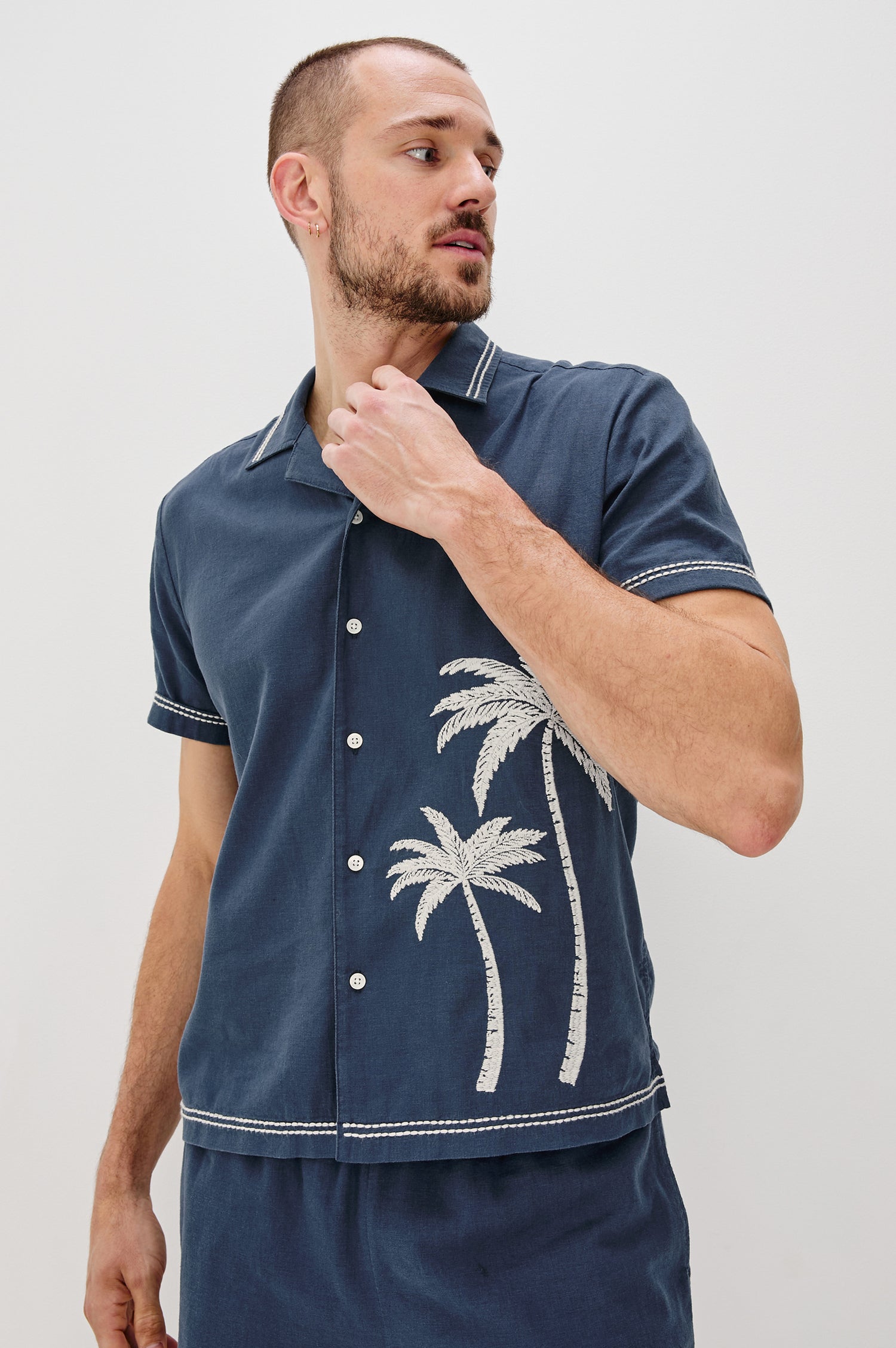 Gibson Button Front Shirt with Open Relaxed Collar, Short Sleeves, White Contrast Buttons, Contrast White Stitching at Collar and Hems and Embroidered White Palm Trees on Left Side in Navy White Palm Colorway. Front View Shown on Model.