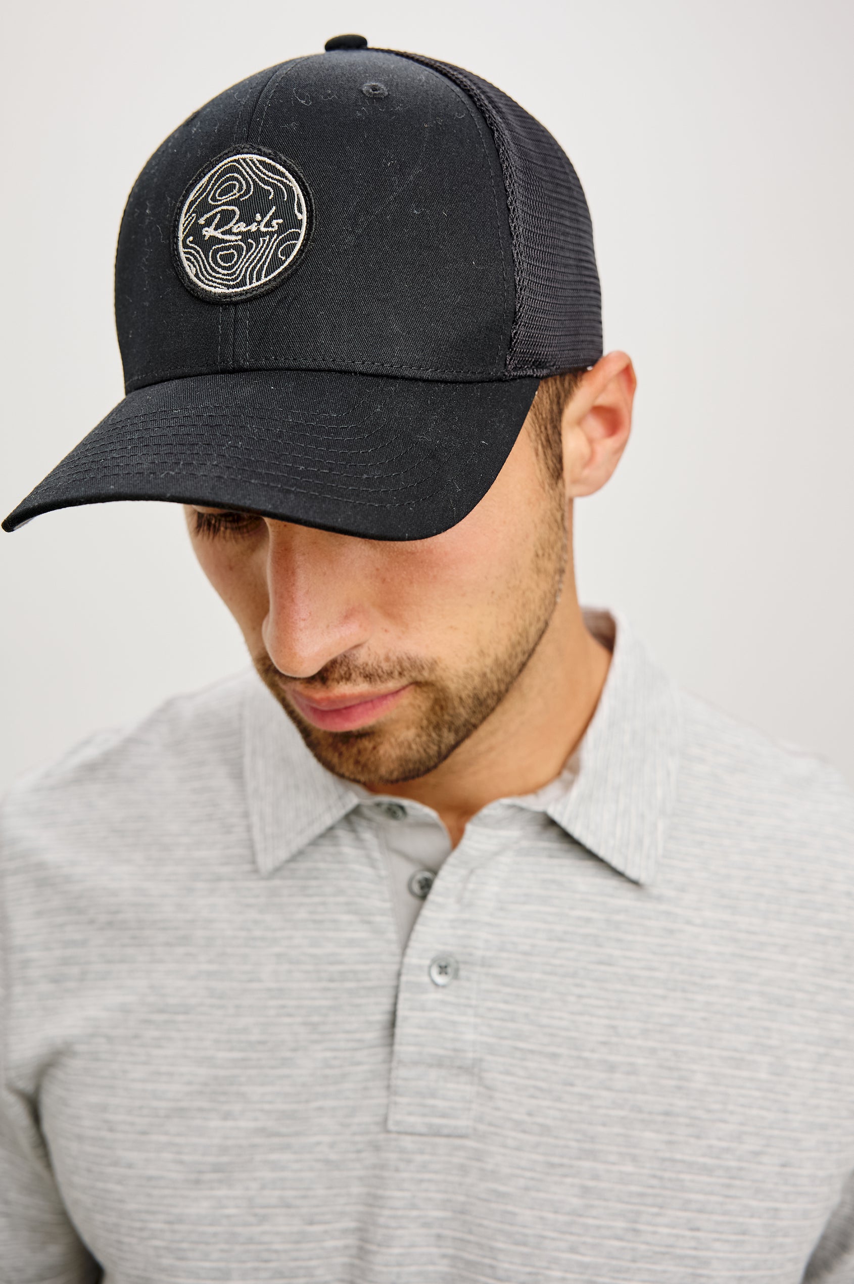 Golf Hat With Embroidered Branded Patch at Front, Adjustable Snapback, Mesh Back, and 6-Panel Construction in Black Colorway - Upper Body Front View Featured on Model