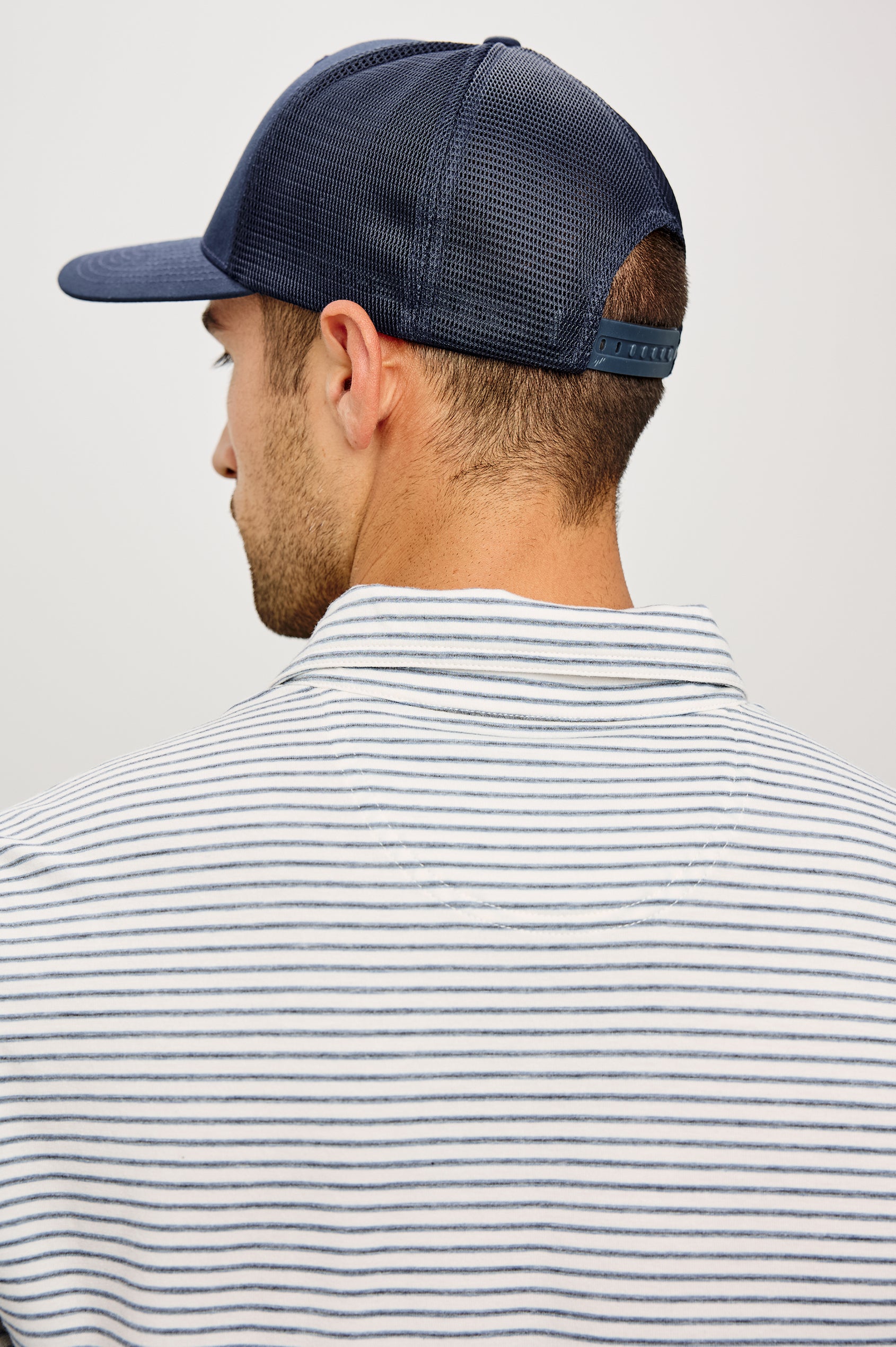 Golf Hat With Embroidered Branded Patch at Front, Adjustable Snapback, Mesh Back, and 6-Panel Construction in Navy Colorway - Upper Body Back View Featured on Model