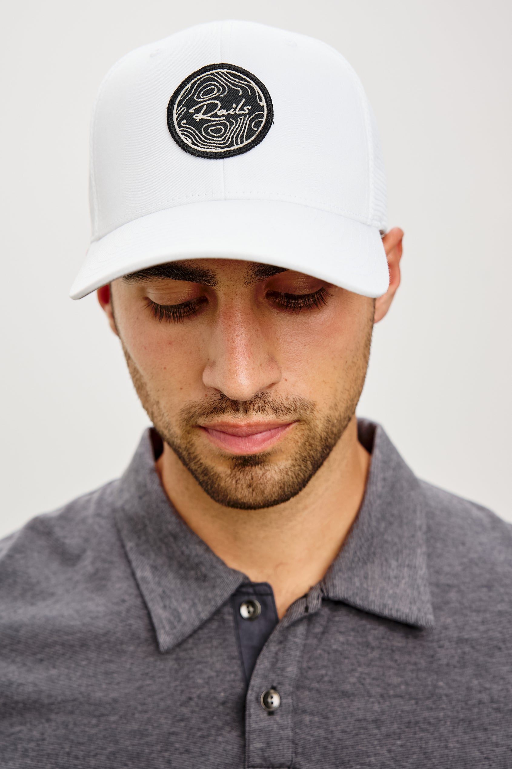Golf Hat With Embroidered Branded Patch at Front, Adjustable Snapback, Mesh Back, and 6-Panel Construction in White Colorway - Upper Body Front View Featured on Model