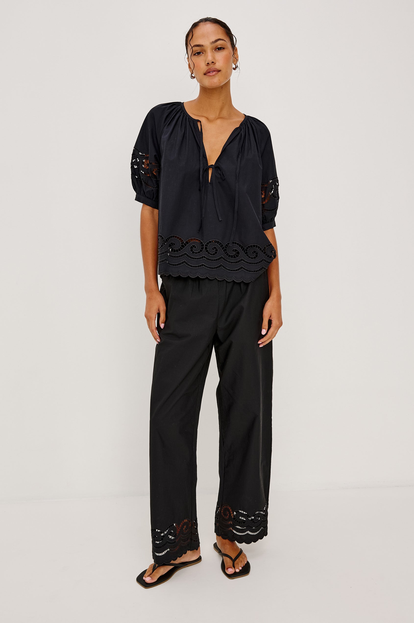 Henrik High-Rise High-Waisted Pant With Wide Smocked Waistband, Side Pockets, Straight Legs, and Scalloped Ladder Embroidered Hem in Black Colorway - Full Body Front View Featured on Model