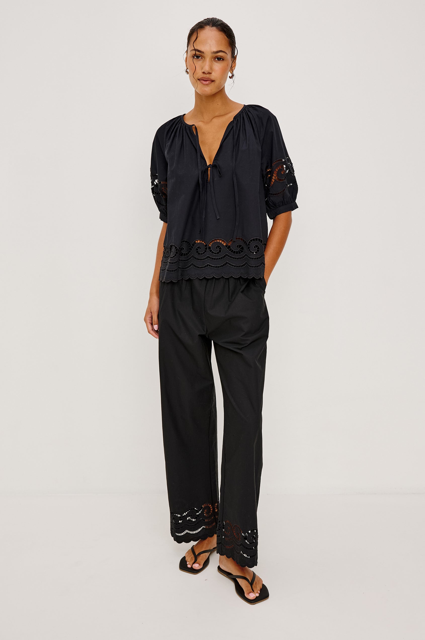 Henrik High-Rise High-Waisted Pant With Wide Smocked Waistband, Side Pockets, Straight Legs, and Scalloped Ladder Embroidered Hem in Black Colorway - Full Body Front View Featured on Model