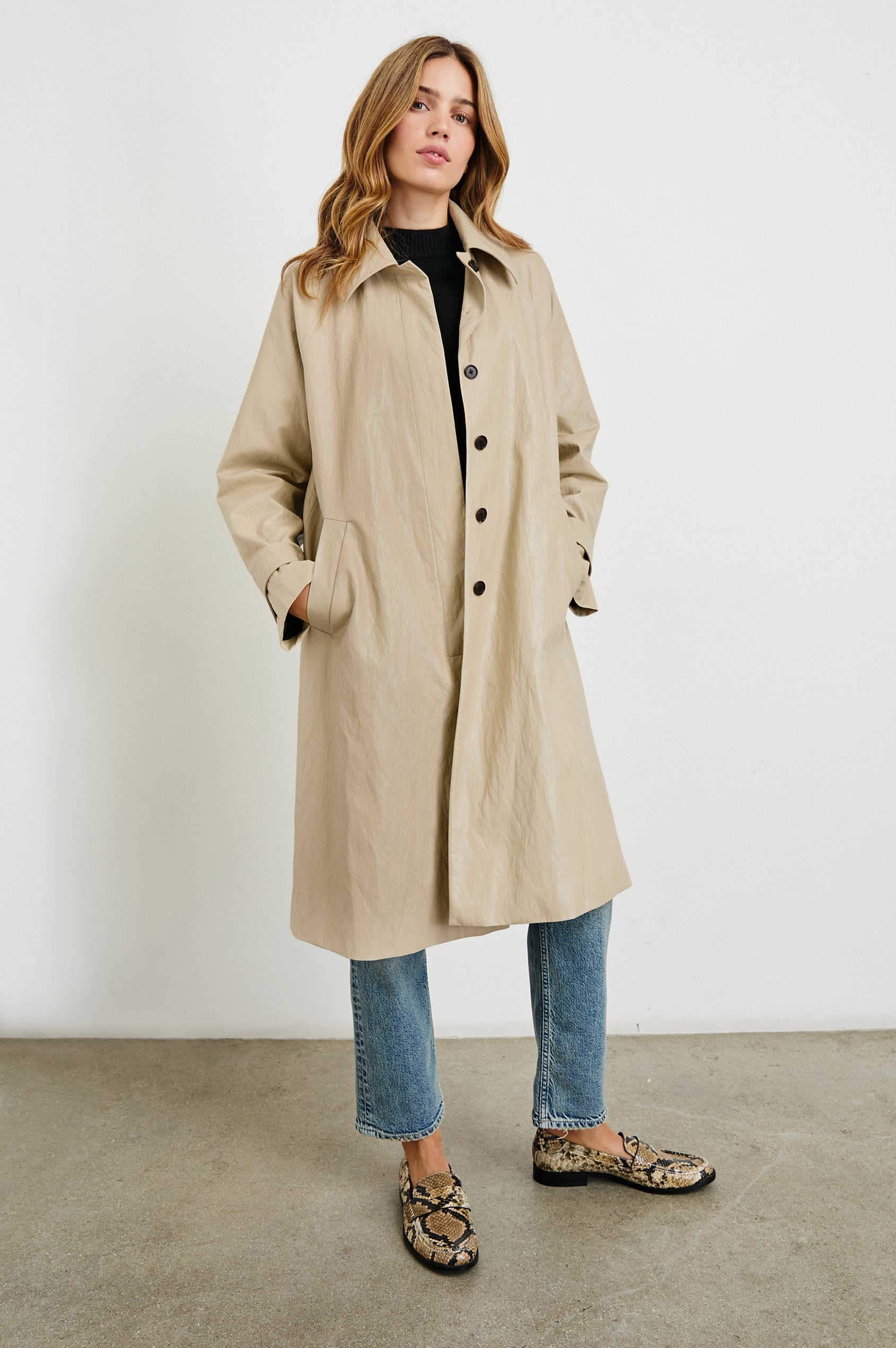 Hills Knee-Length Faux Leather Jacket with Button Closure, a Hidden Placket, Two Front Pockets, and Button Tabs at the Cuffs in Dune Colorway - Front Full Body View Featured on Model 