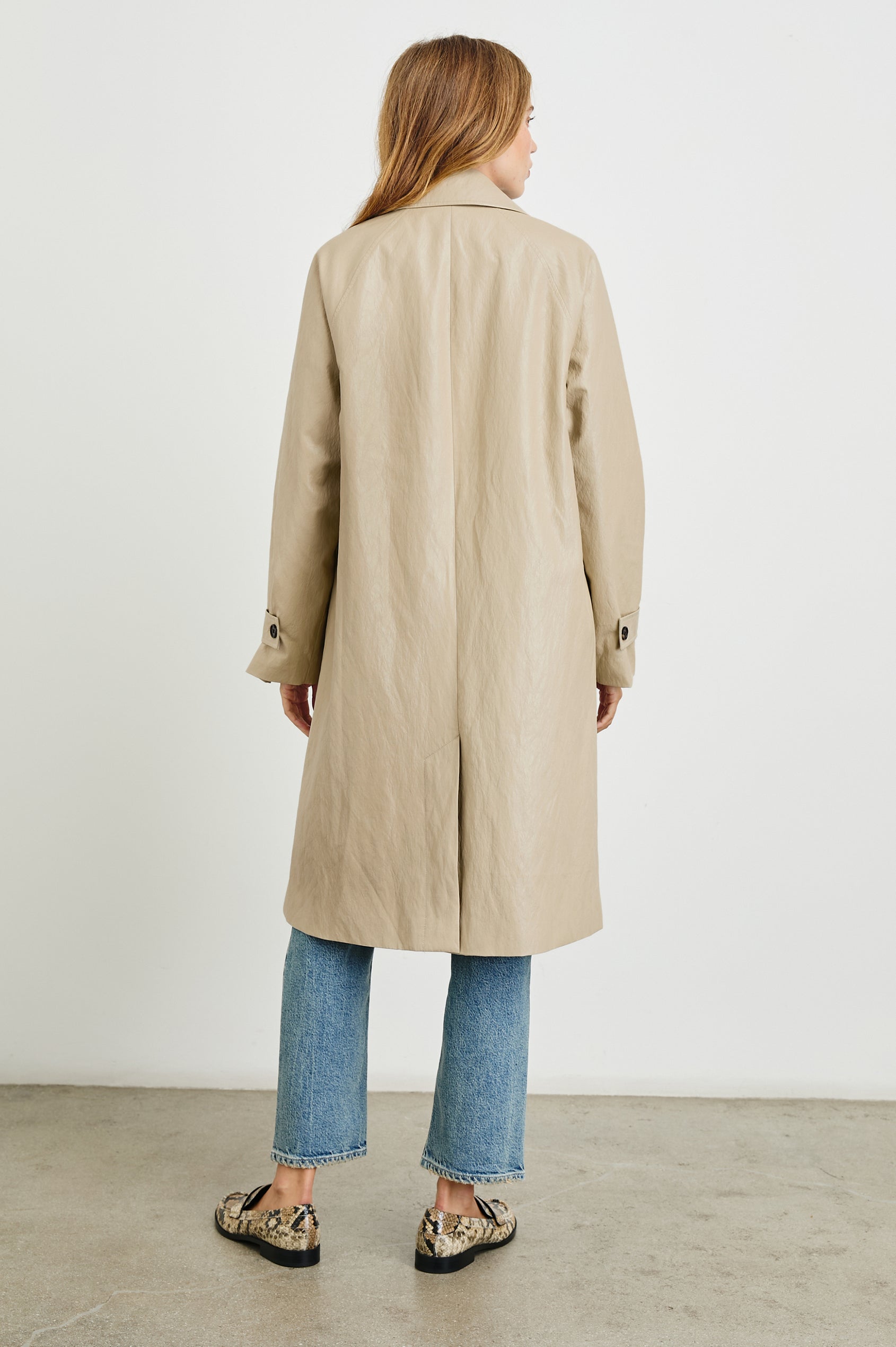 Hills Knee-Length Faux Leather Jacket with Button Closure, a Hidden Placket, Two Front Pockets, and Button Tabs at the Cuffs in Dune Colorway - Back Full Body View Featured on Model 