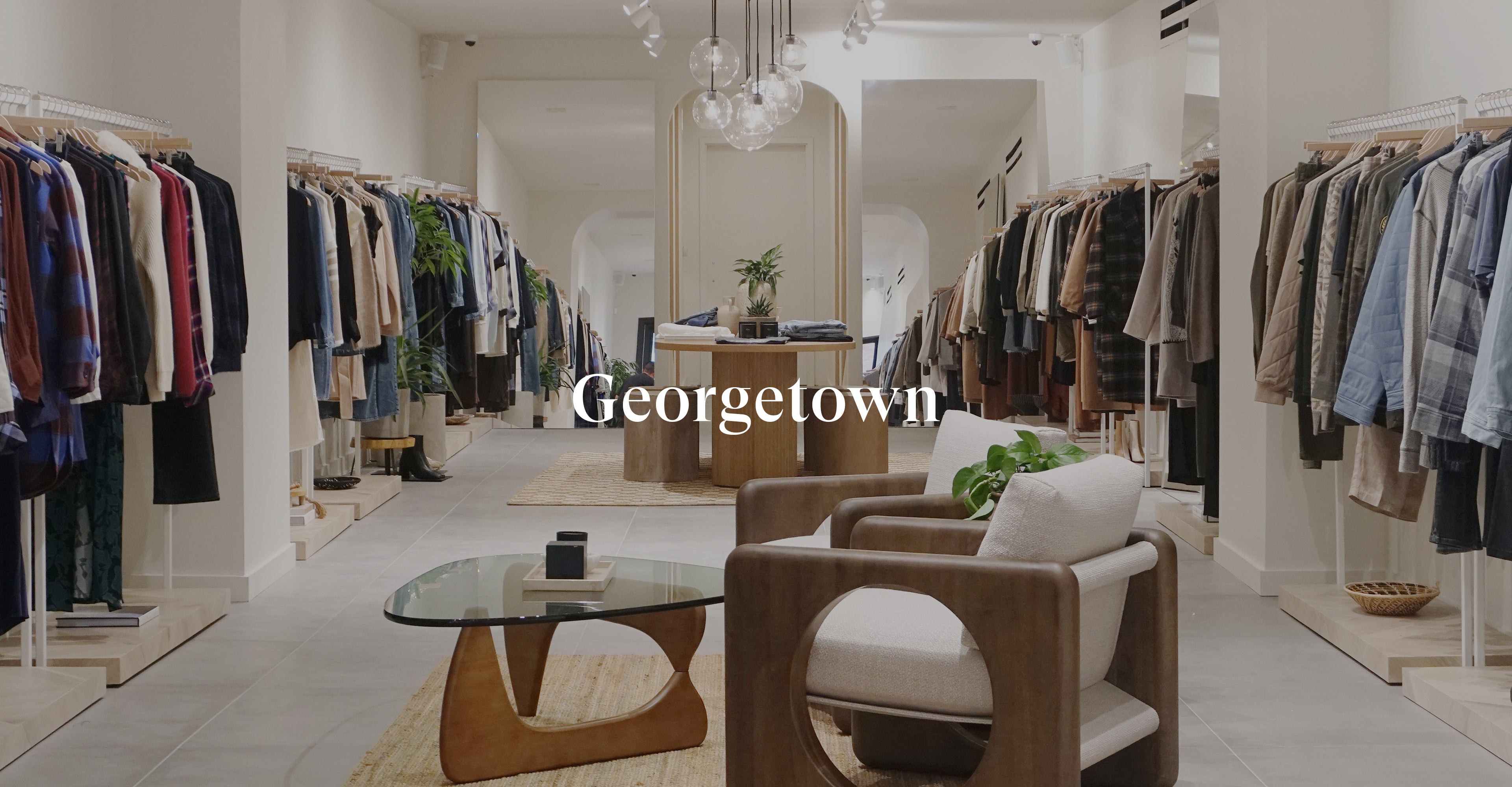 INSIDE OF GEORGETOWN STORE SHOWING ONE ROOM WITH MULTIPLE CLOTHING RACKS OF CLOTHING AGAINST EACH WALL AND TWO CHAIRS IN THE CENTER OF THE ROOM
