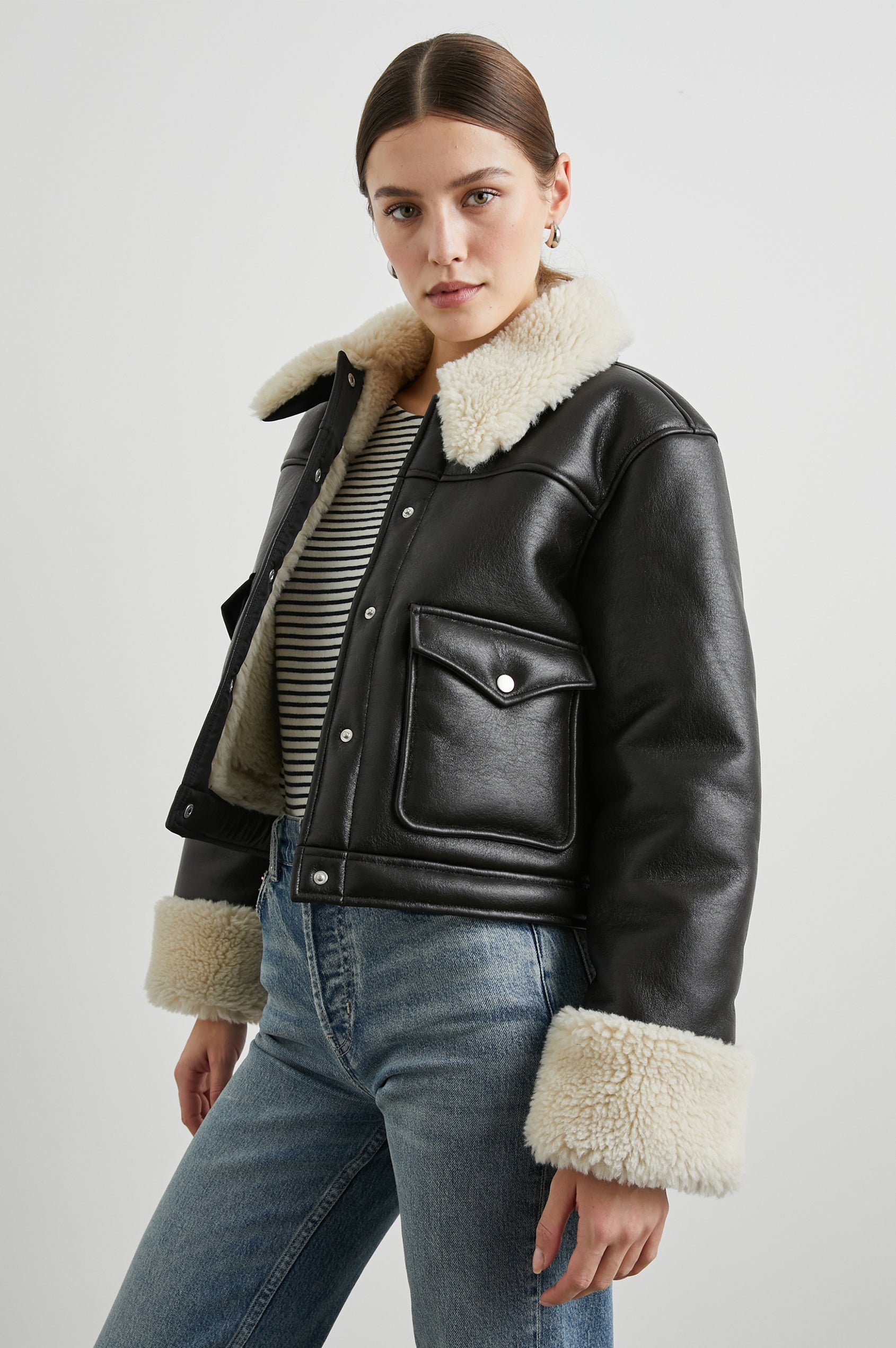 Imani Cropped Faux Leather Jacket with Silver-Toned Snap Closure, Two Front Snap Flap Pockets and Ivory Faux Shearling Lining, Collar and Cuffs in Black Ivory Colorway - Front View Featured on Model  