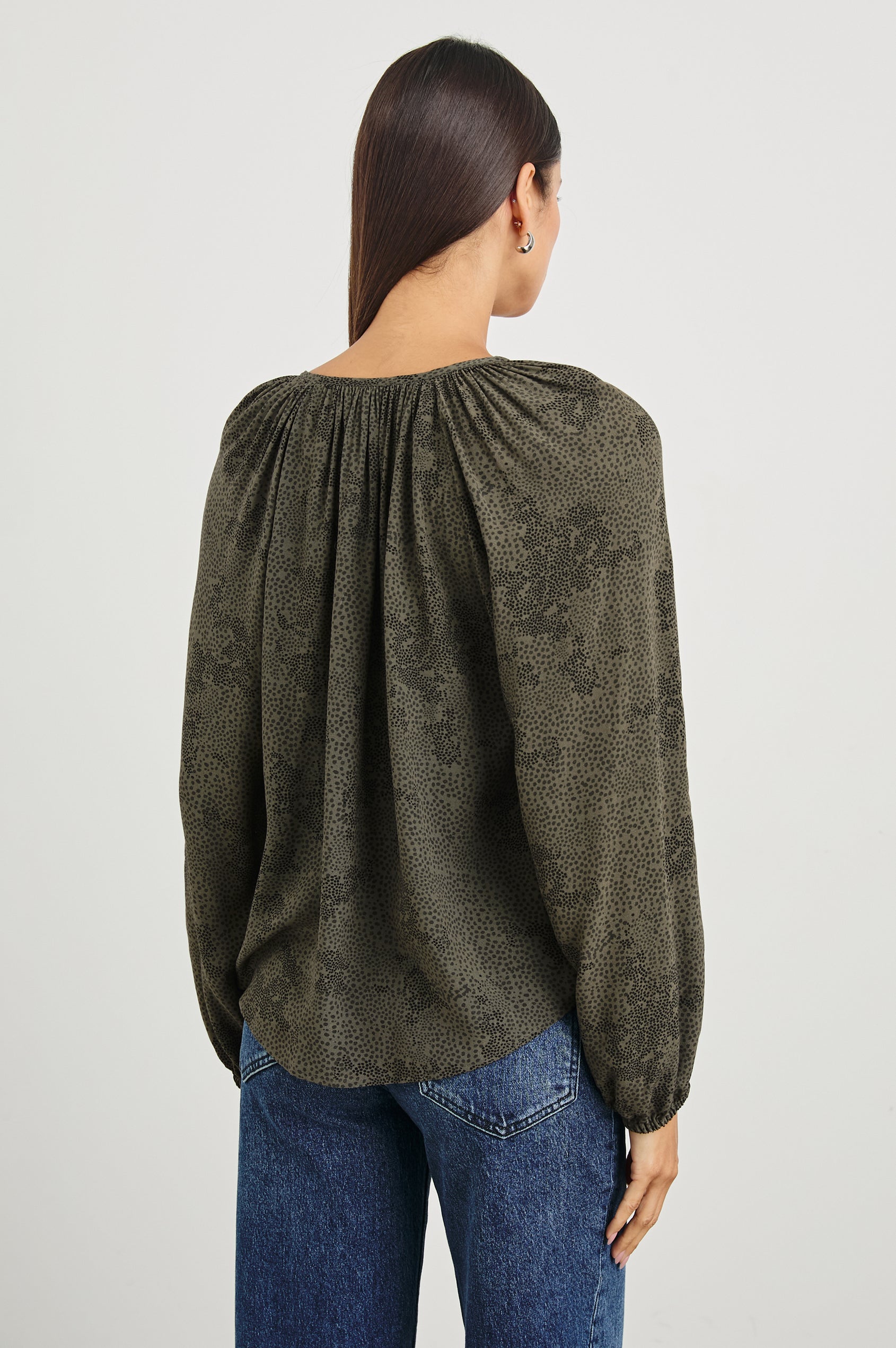 Indi Top with a V Neckline with a Button Placket, Pleating at Back Neckline and Elastic Cuffs in Olive Pebble Colorway, with black pebbles on olive - Back Untucked View Featured on Model