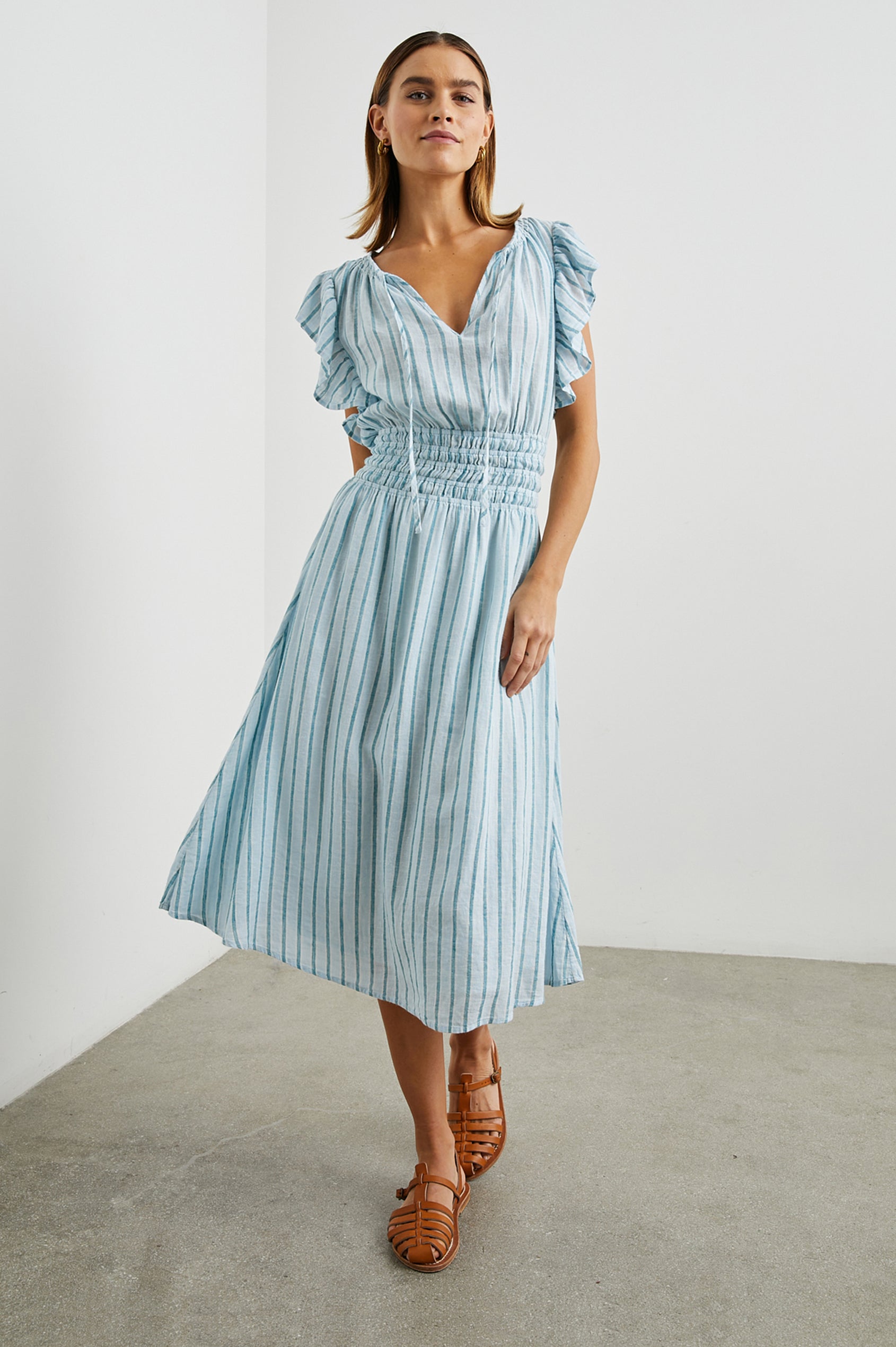 Iona Short Sleeve Midi Dress with Flutter Sleeves, a Deep V Neck with Ties, and a Shirred Waist in Cambria Stripe Colorway, Vertical Stripes in White, Blue and Light Blue - Front Full Body View Featured on Model 