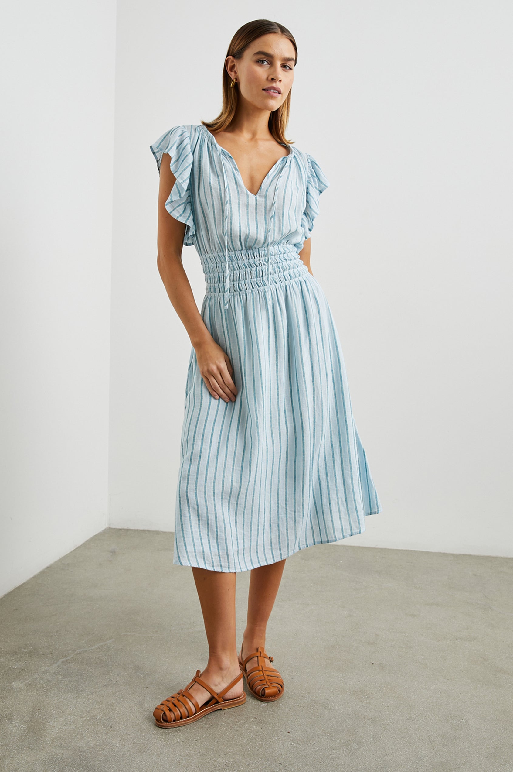 Iona Short Sleeve Midi Dress with Flutter Sleeves, a Deep V Neck with Ties, and a Shirred Waist in Cambria Stripe Colorway, Vertical Stripes in White, Blue and Light Blue - Front Full Body View Featured on Model 