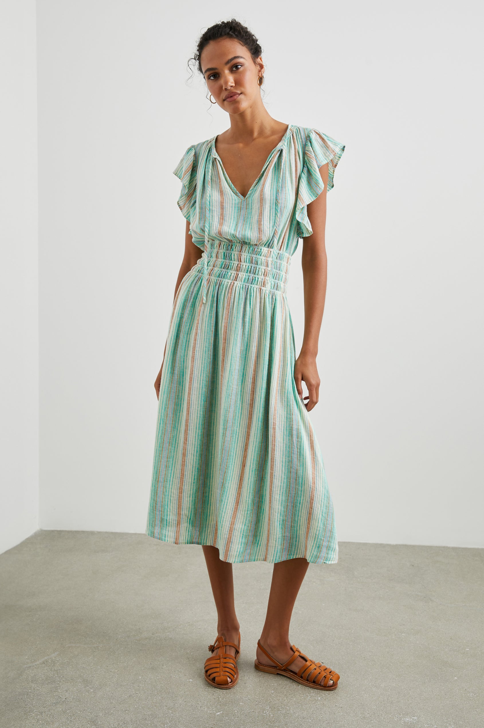 Iona Short Sleeve Midi Dress with Flutter Sleeves, a Deep V Neck with Ties, and a Shirred Waist in Seaview Stripe Colorway, Vertical Stripes in Browns, Blues and Creams - Front Full Body View Featured on Model 