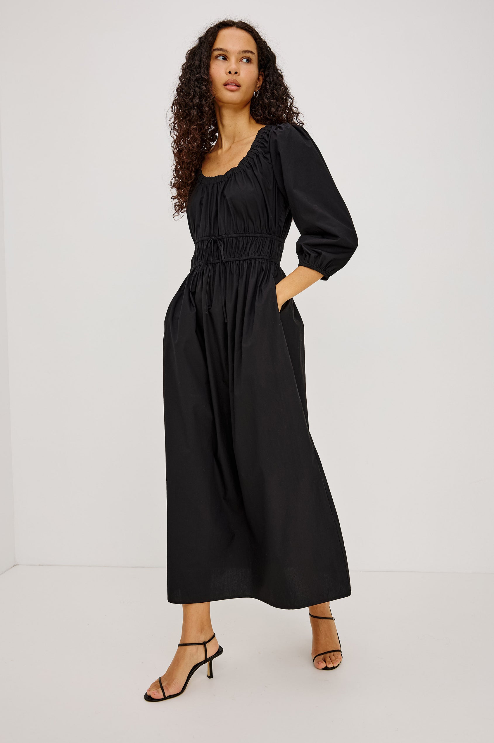 Isabelle Maxi Dress in Cotton Poplin With Ruched Scoop Neck, Puff Elbow-Length Sleeves, and Laddered Shirred Waist With Ties in Black Colorway - Full Body Front View Featured on Model