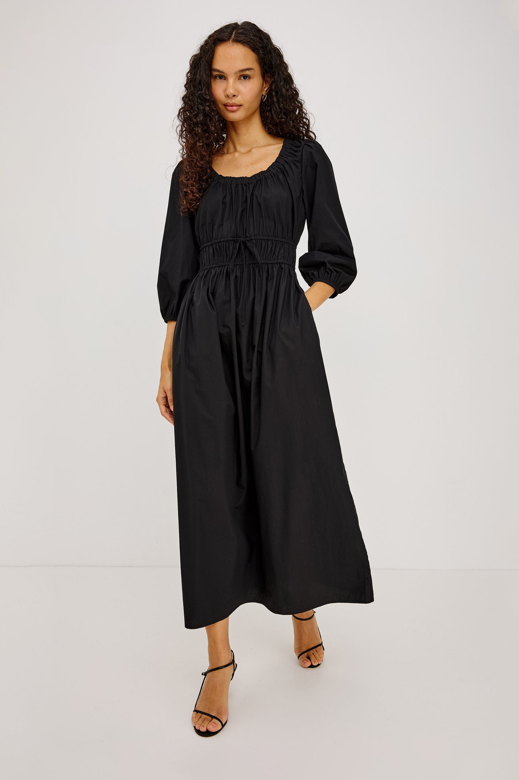 Isabelle Maxi Dress in Cotton Poplin With Ruched Scoop Neck, Puff Elbow-Length Sleeves, and Laddered Shirred Waist With Ties in Black Colorway - Full Body Front View Featured on Model