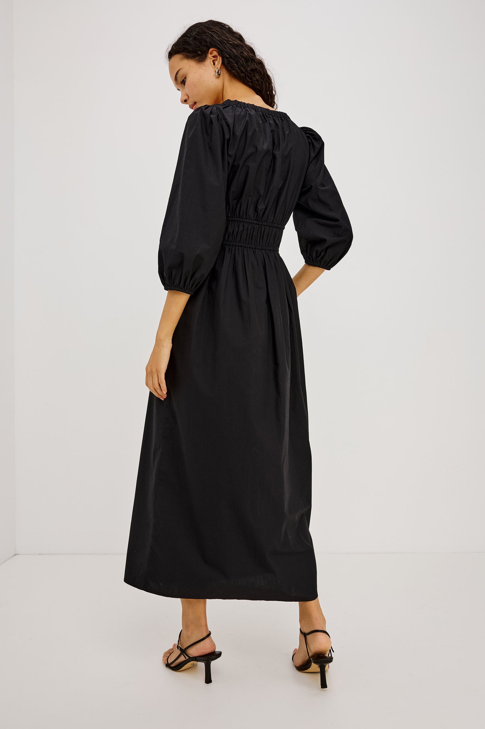 Isabelle Maxi Dress in Cotton Poplin With Ruched Scoop Neck, Puff Elbow-Length Sleeves, and Laddered Shirred Waist With Ties in Black Colorway - Full Body Back View Featured on Model